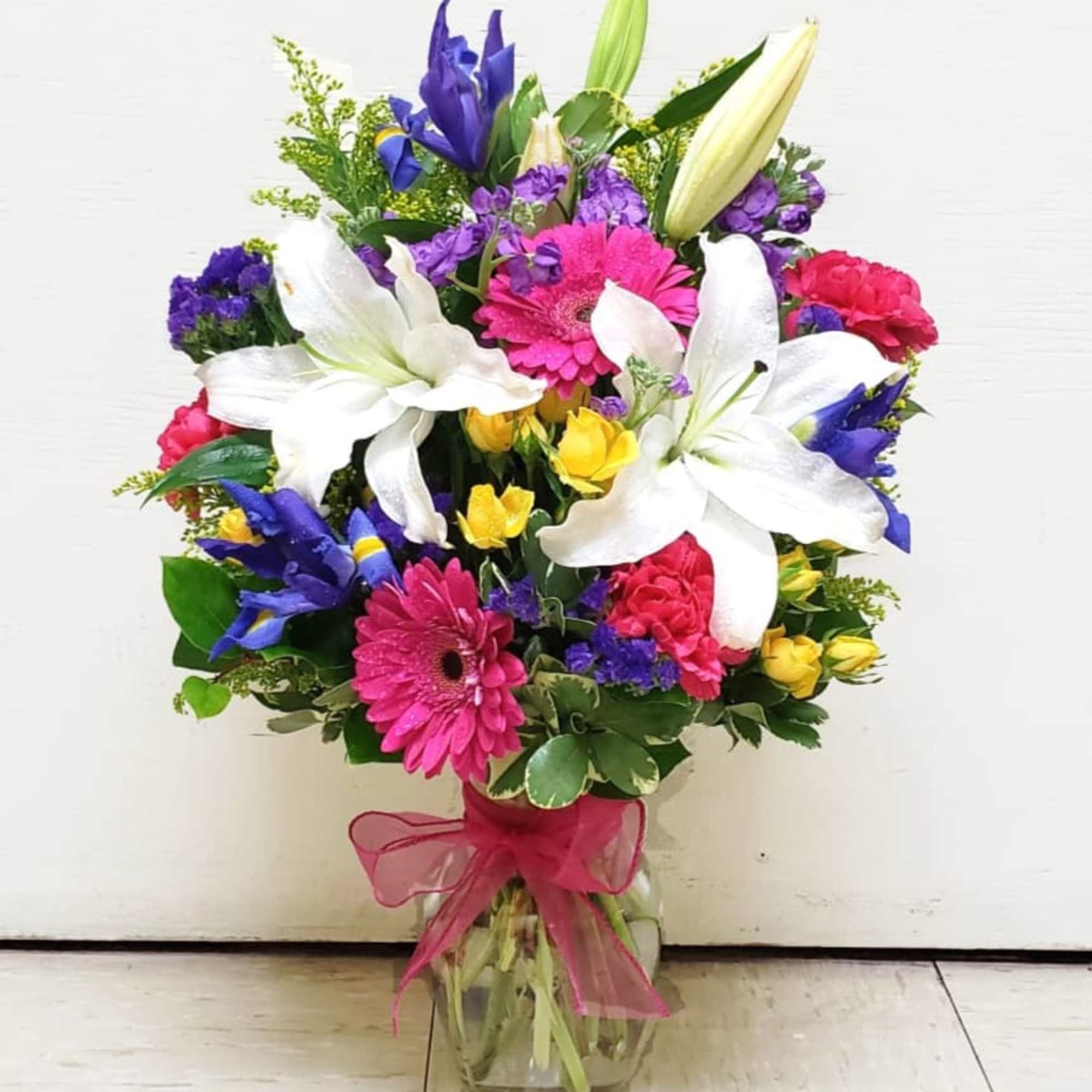 Mixed bouquet with white lilies, pink gerberas, and purple flowers in a glass vase