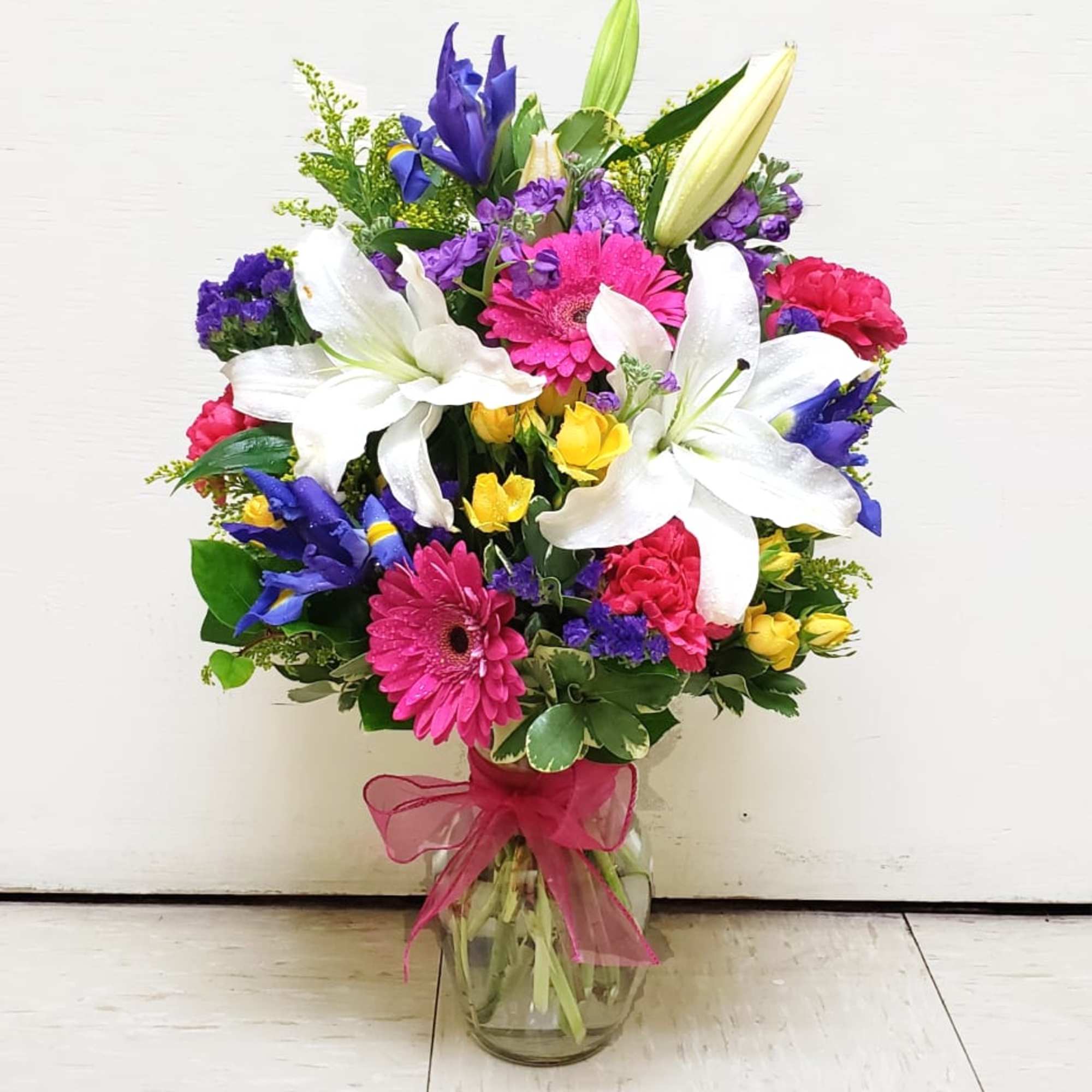 Colorful bouquet with white lilies, pink gerberas, and blue irises in a glass vase