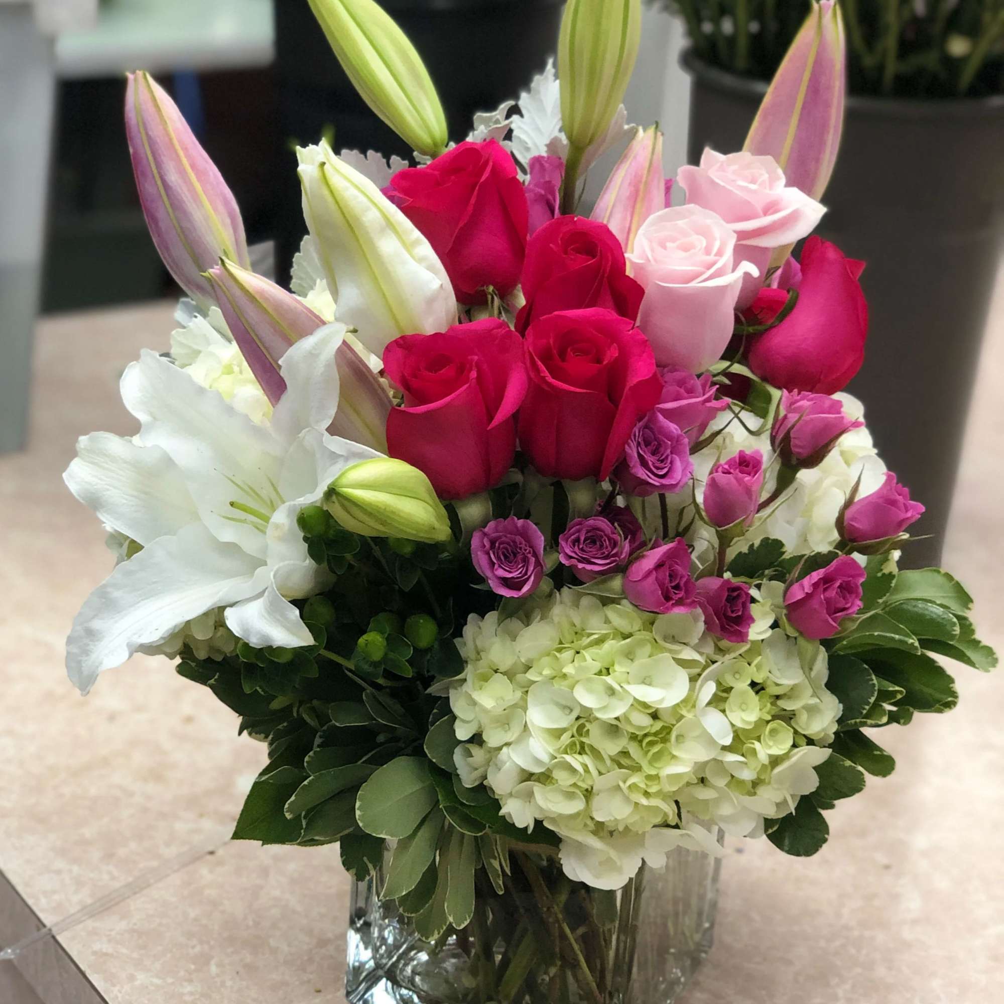 Pink and white rose bouquet with lilies and hydrangea in a square glass vase