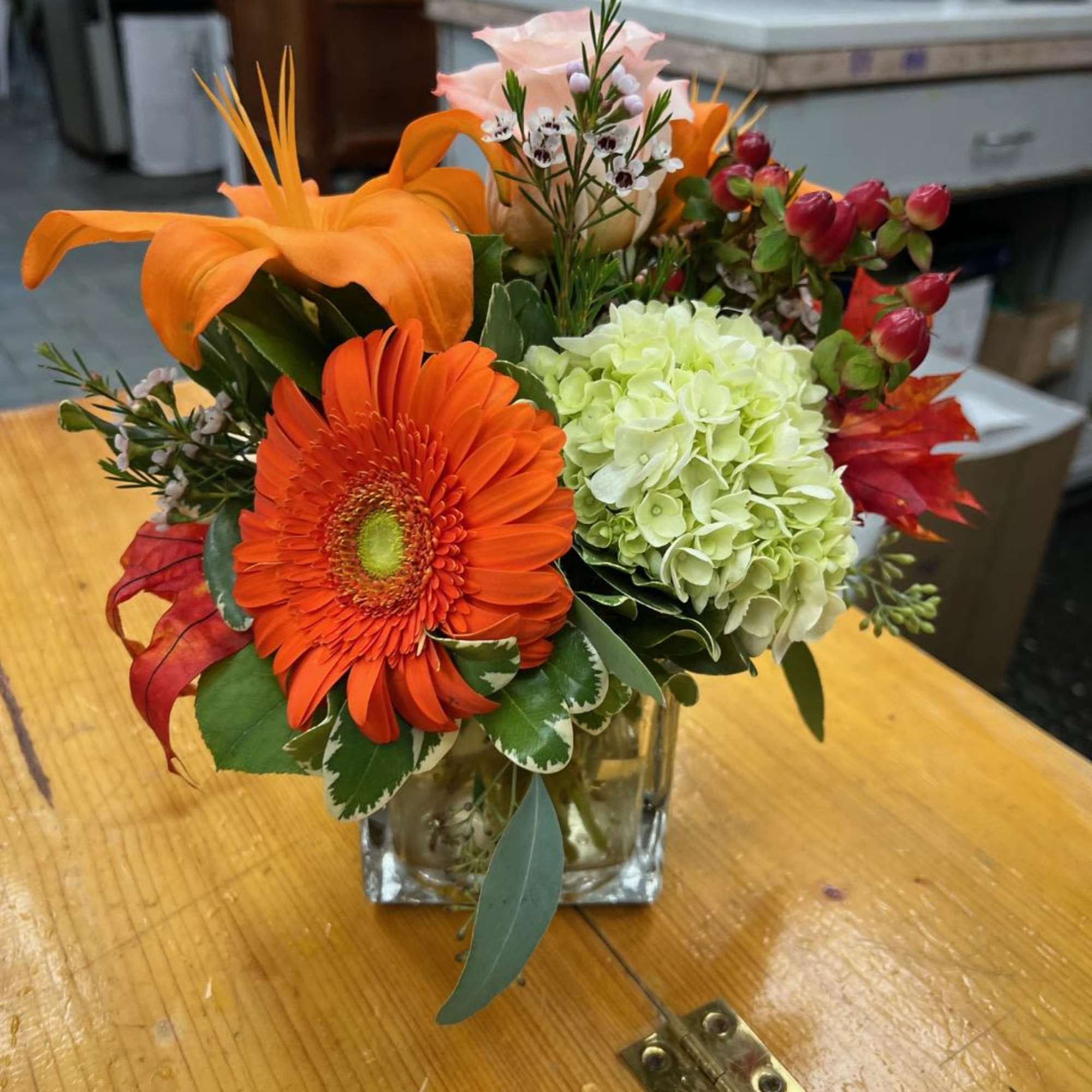 Mixed bouquet in a square glass vase with orange and pink blooms