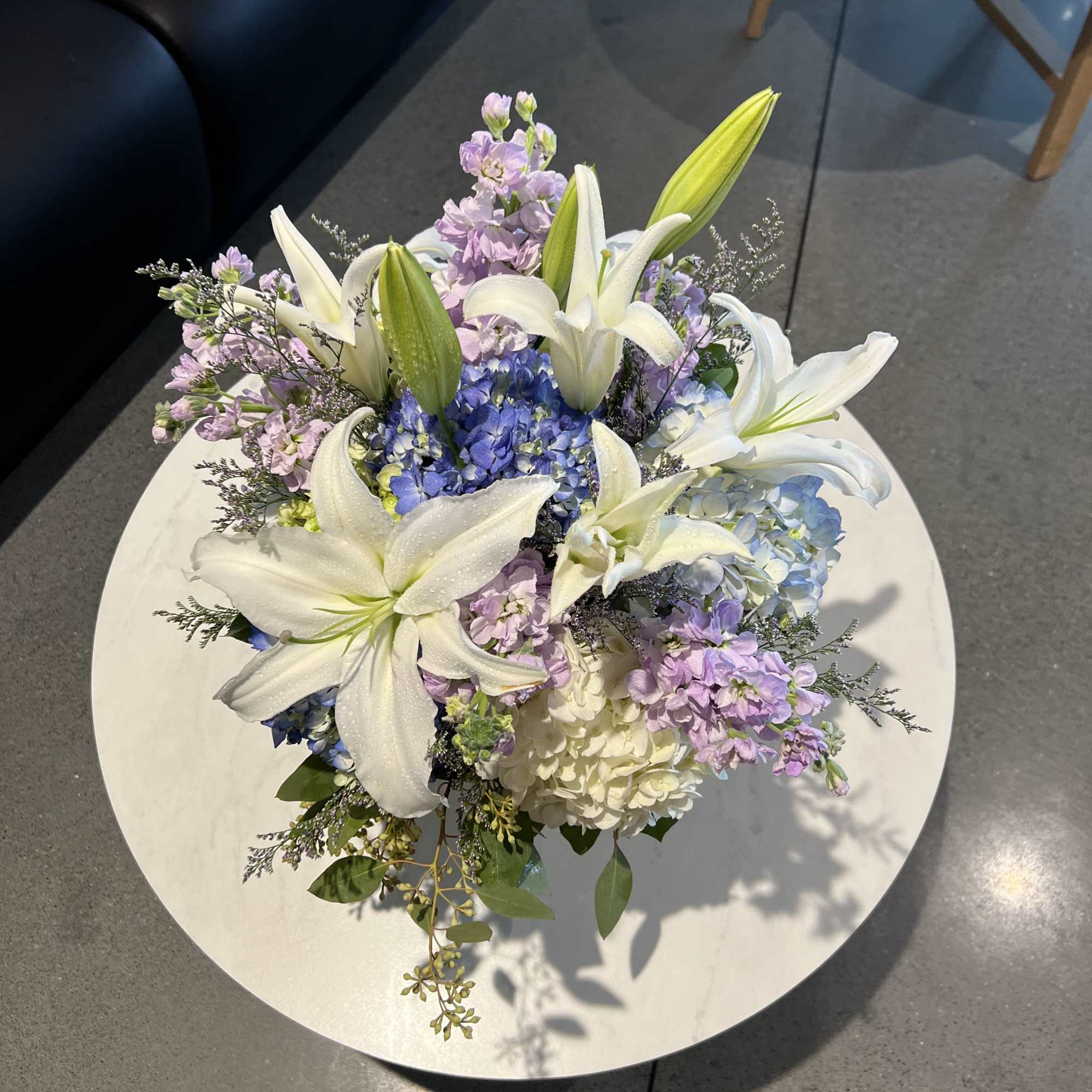 Bouquet of white lilies, blue hydrangeas, and lavender flowers on a round table