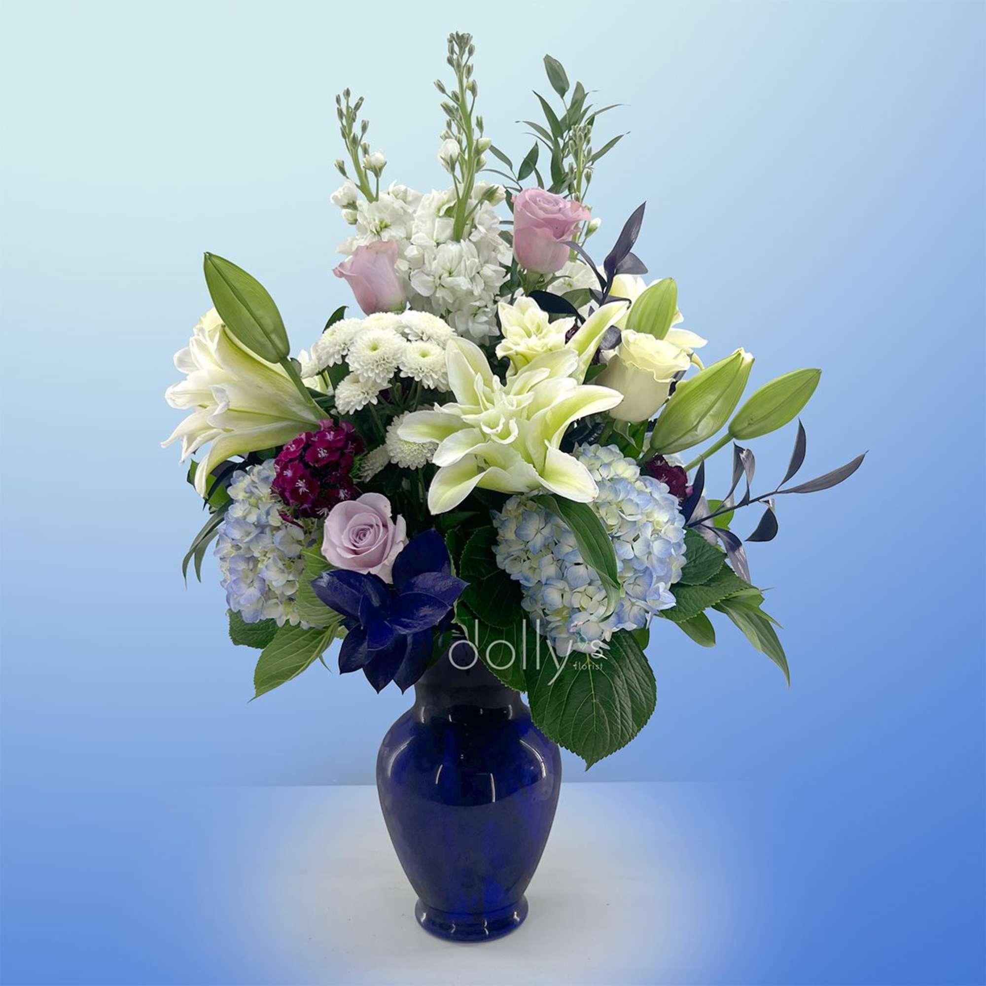 Pale blue hydrangeas and large white lilies create a serene, elegant centerpiece, photo 2 of 2