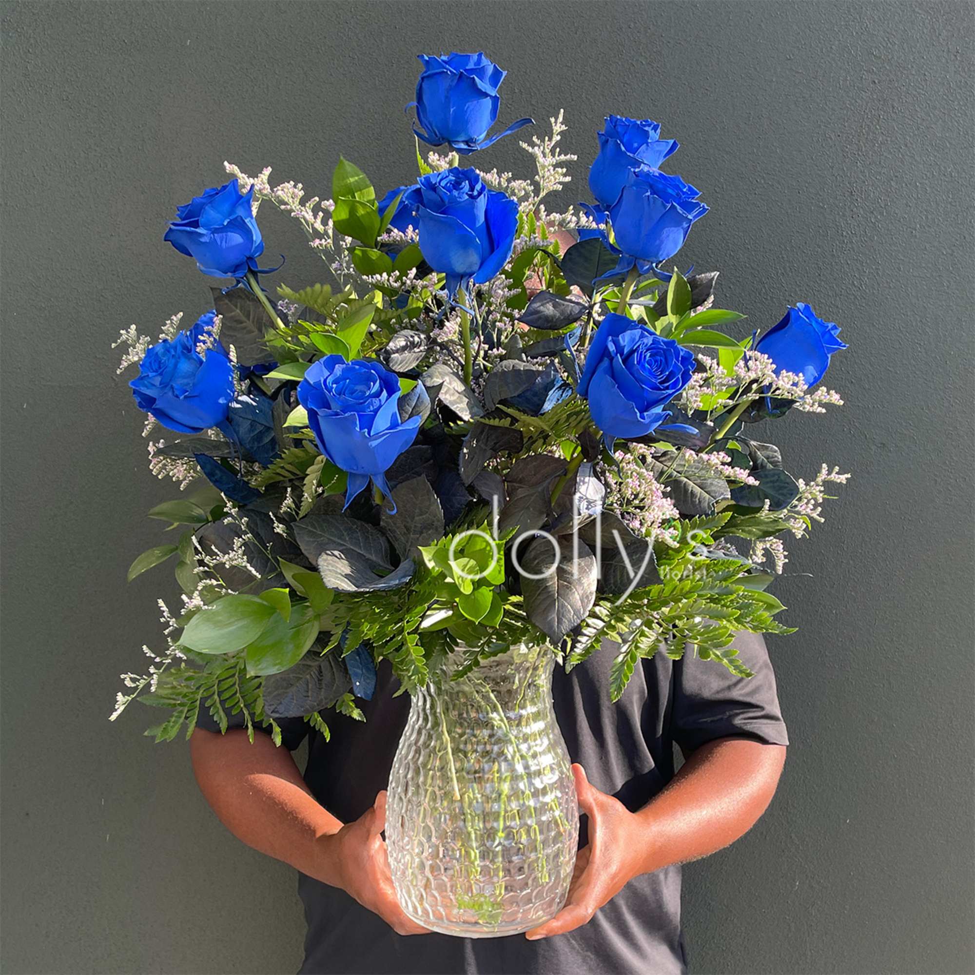 Blue roses arranged in a clear glass vase with mixed greenery