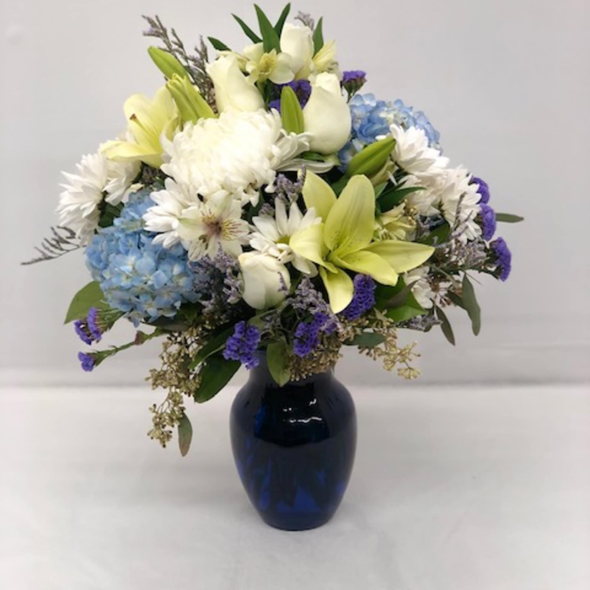 White and blue floral arrangement in a dark blue vase
