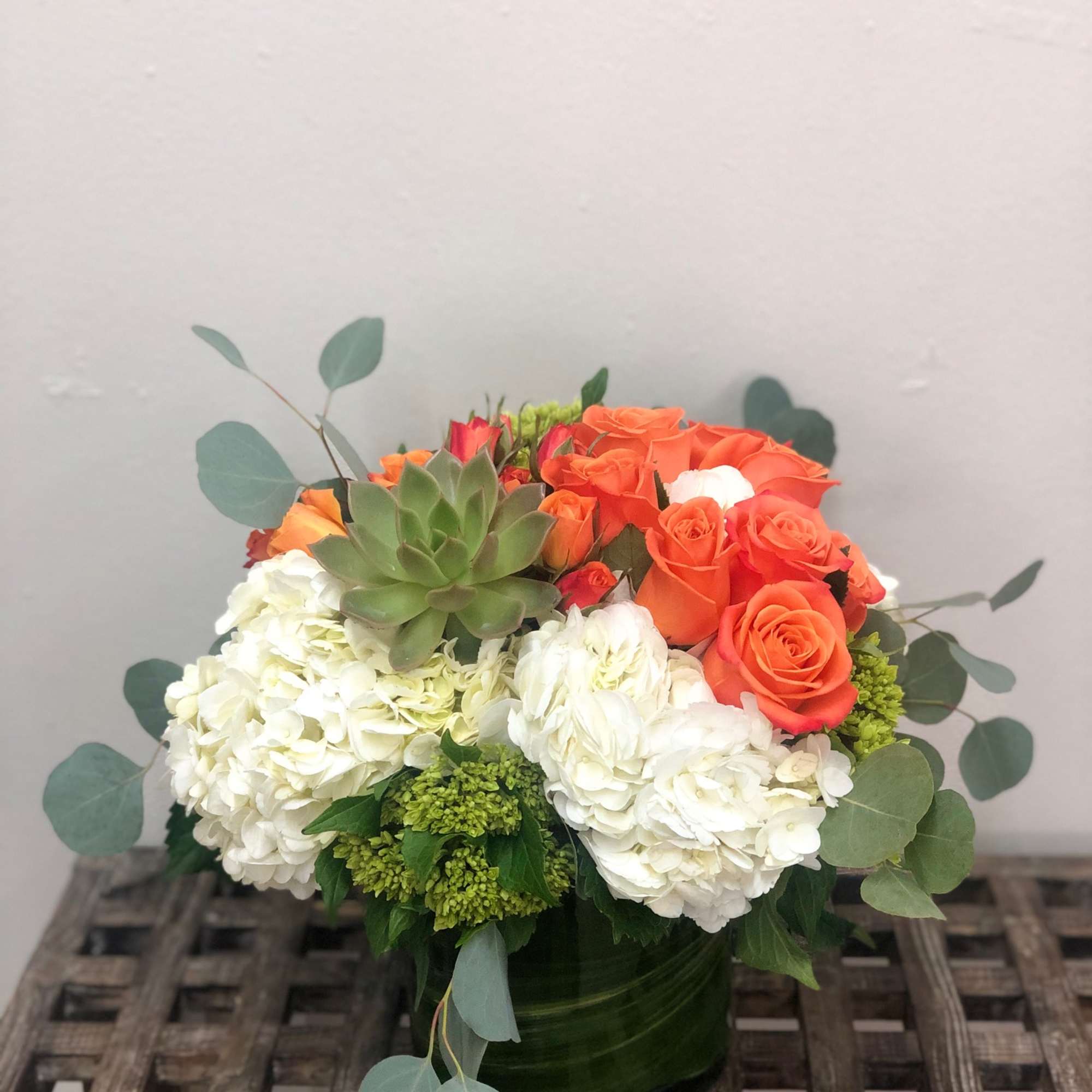 Orange roses and white hydrangeas in a low glass vase with a succulent