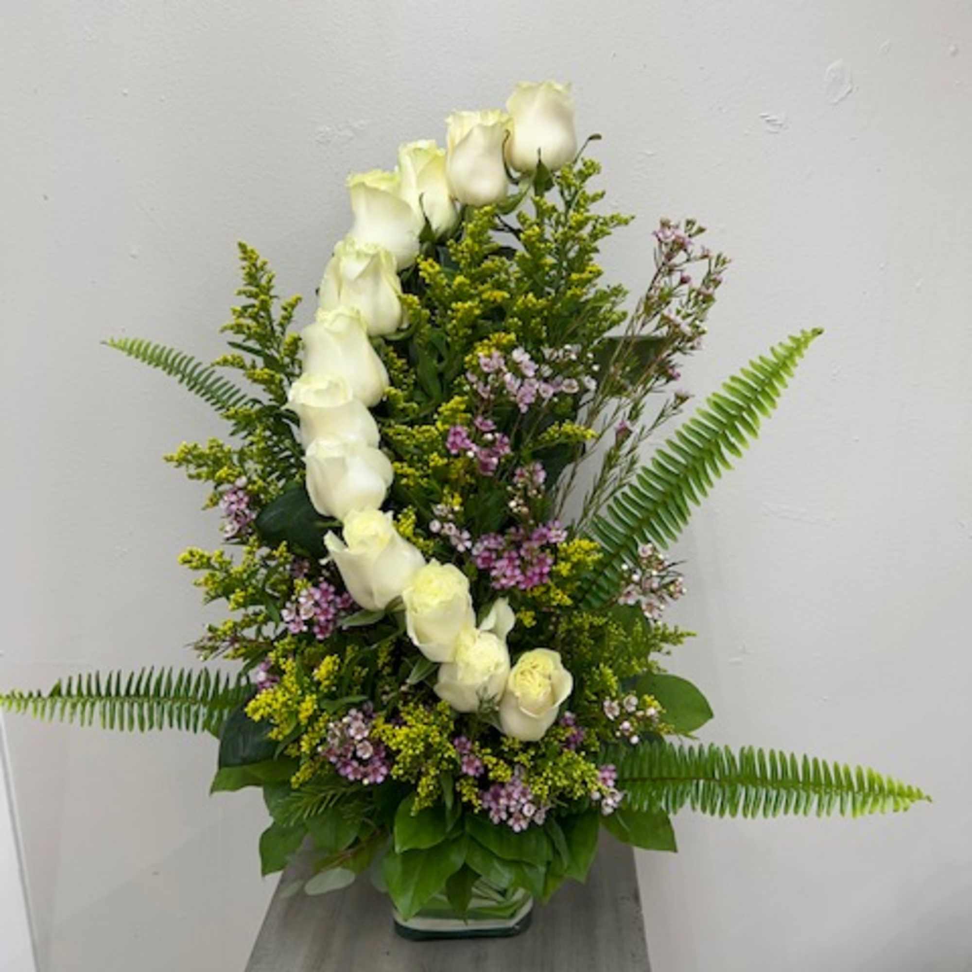 Tall arrangement of white roses with small purple flowers in a glass vase