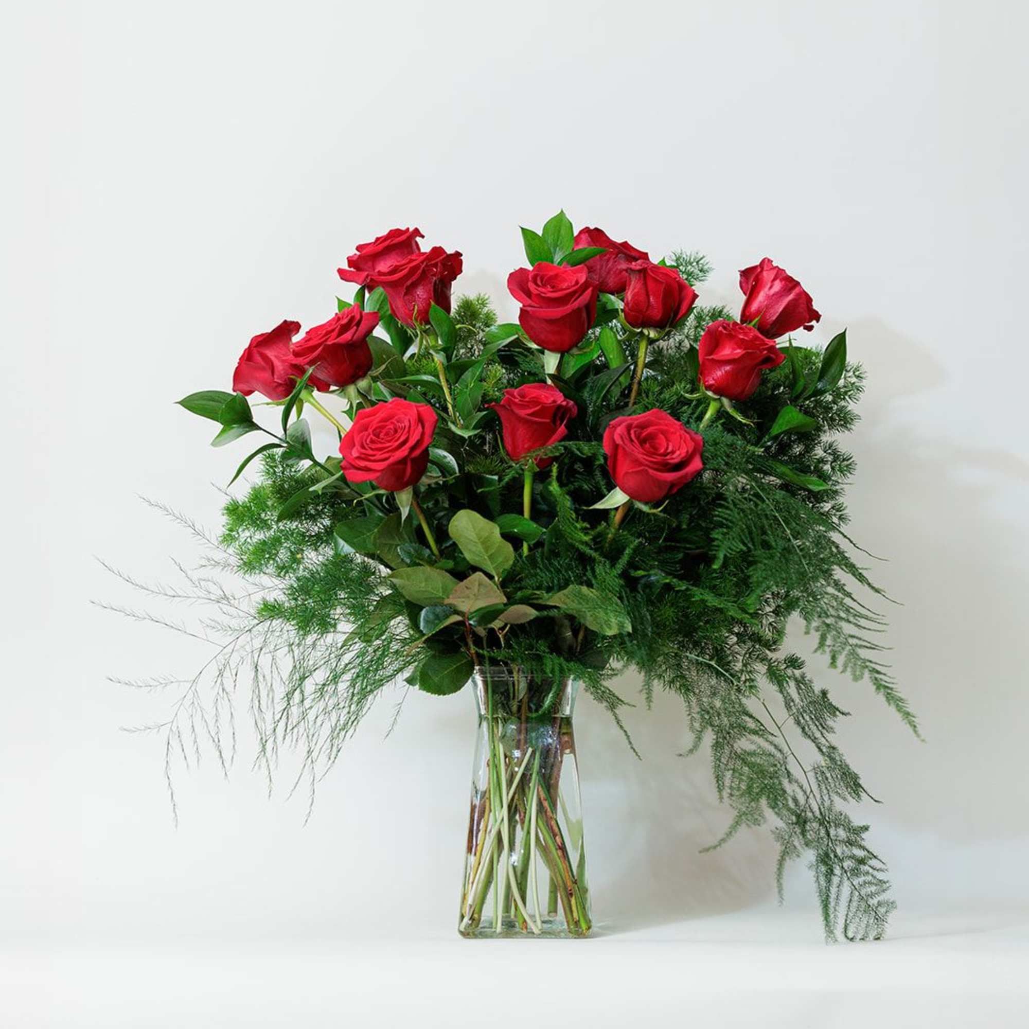Red roses arranged in a clear glass vase with airy greenery, photo 2 of 2