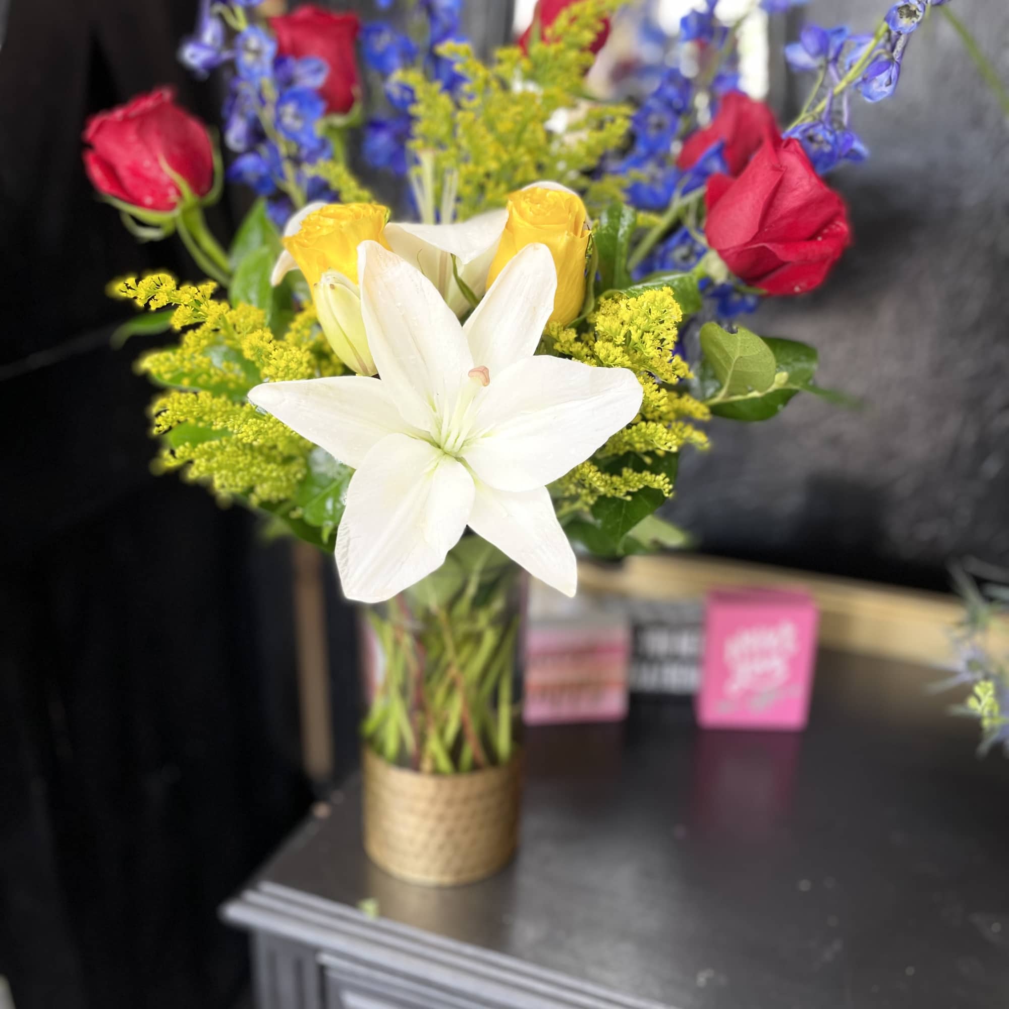 Bouquet of white lilies, yellow roses, red roses, and blue delphinium in a glass vase