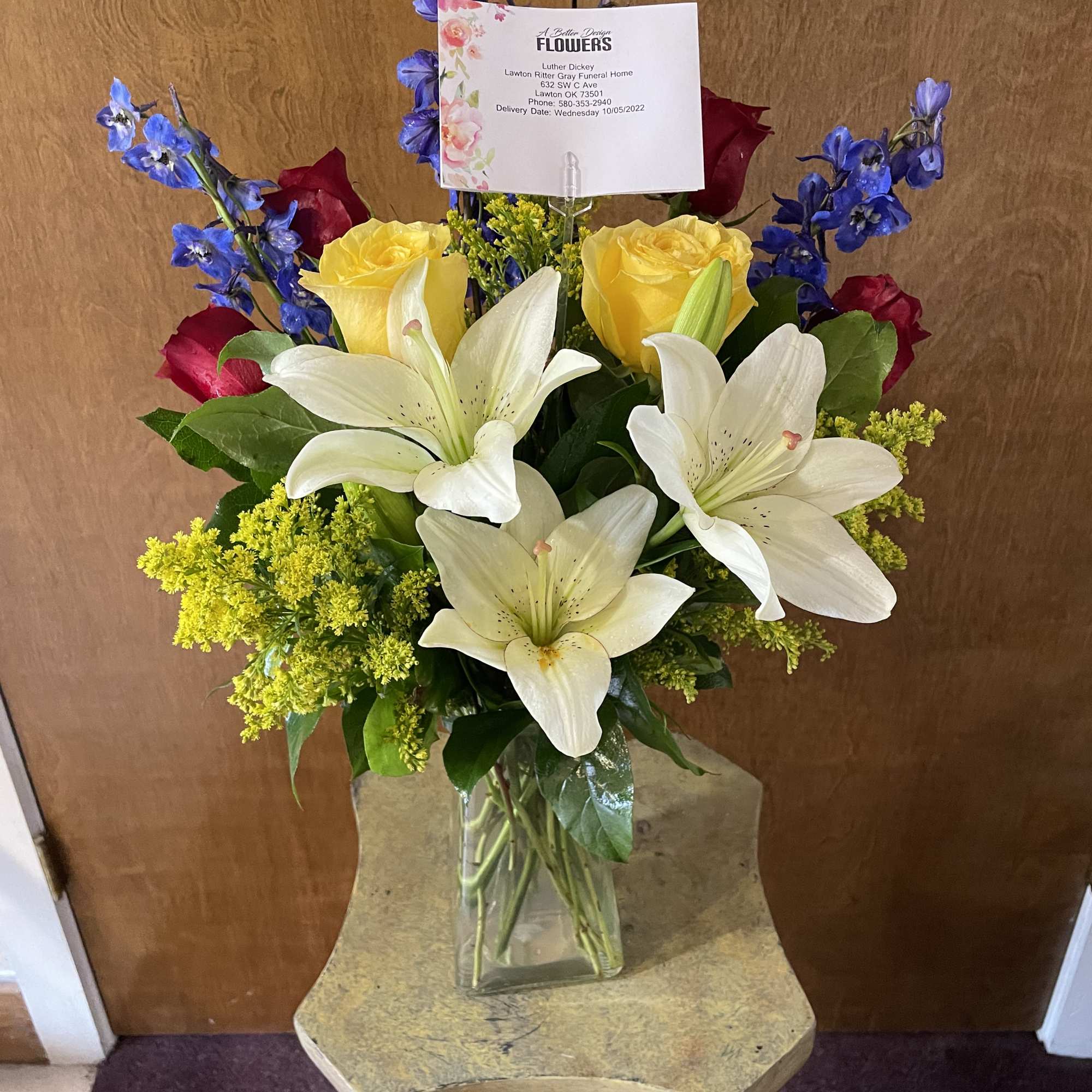 Bouquet of white lilies, yellow roses, and blue delphinium in a glass vase