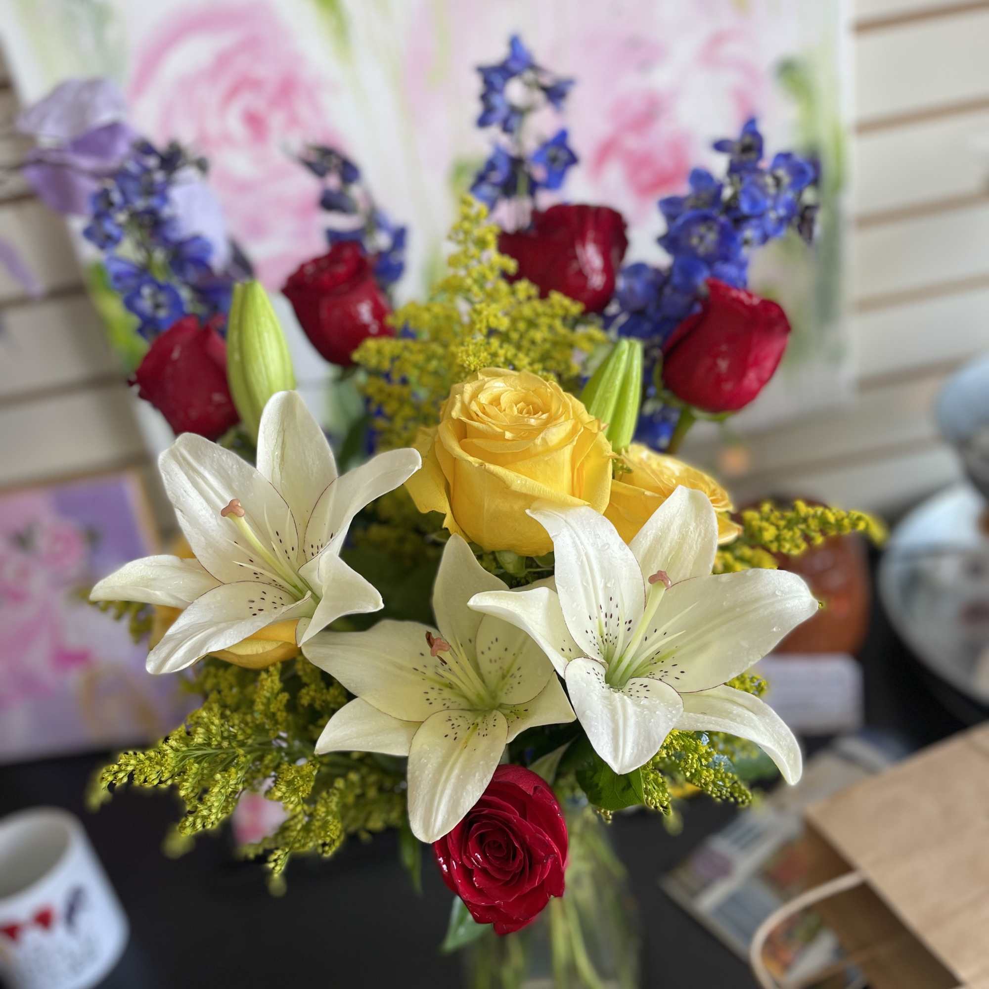 Bouquet of white lilies, yellow and red roses, and blue flowers in a glass vase