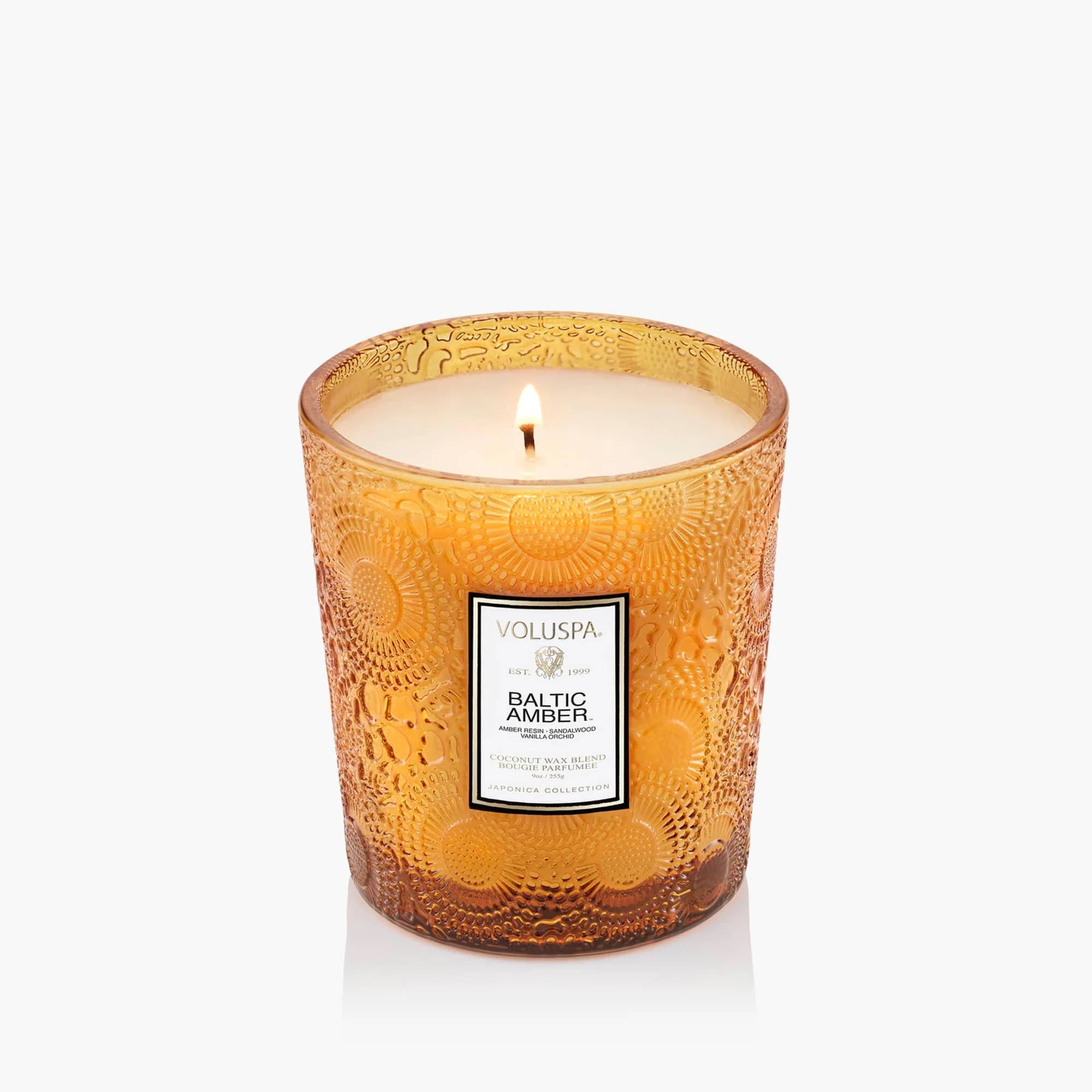 Amber glass candle in a patterned tumbler with a lit wick