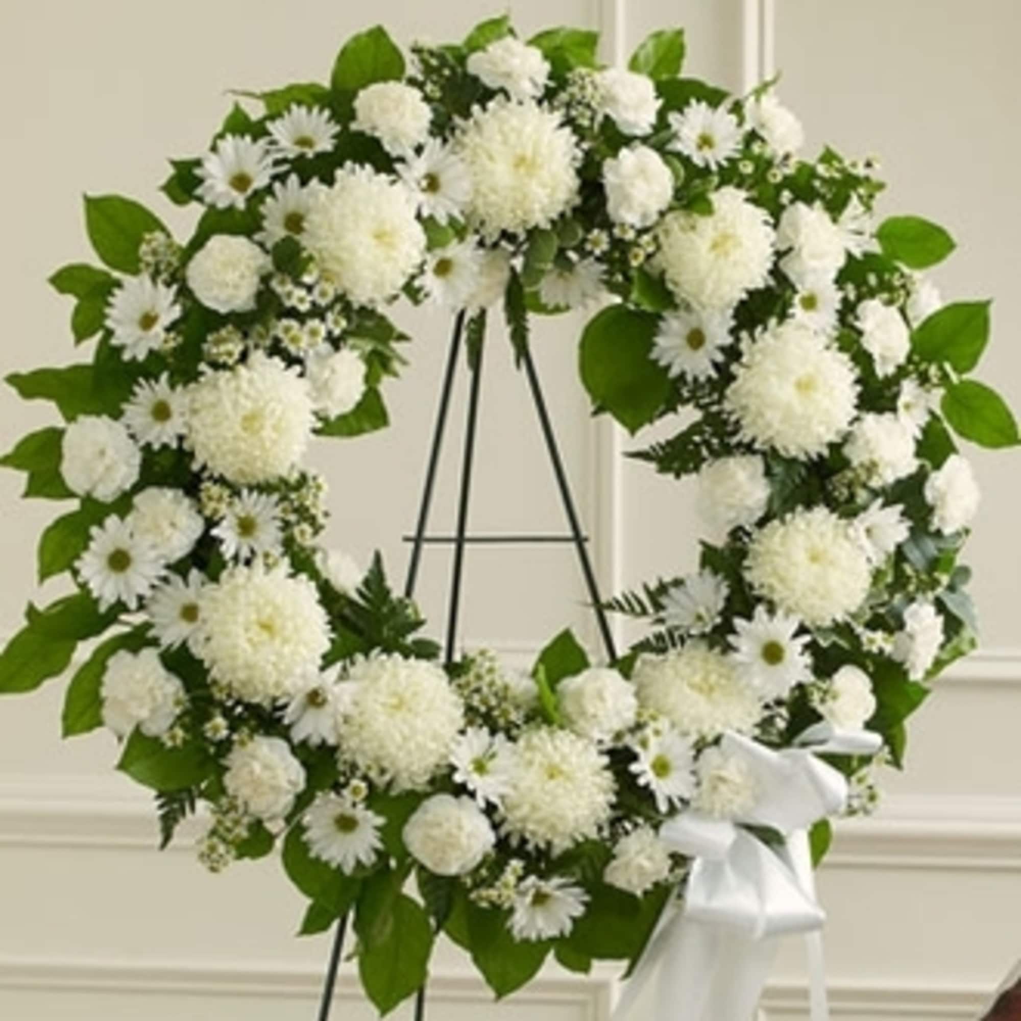 White floral wreath on a black easel with a white ribbon