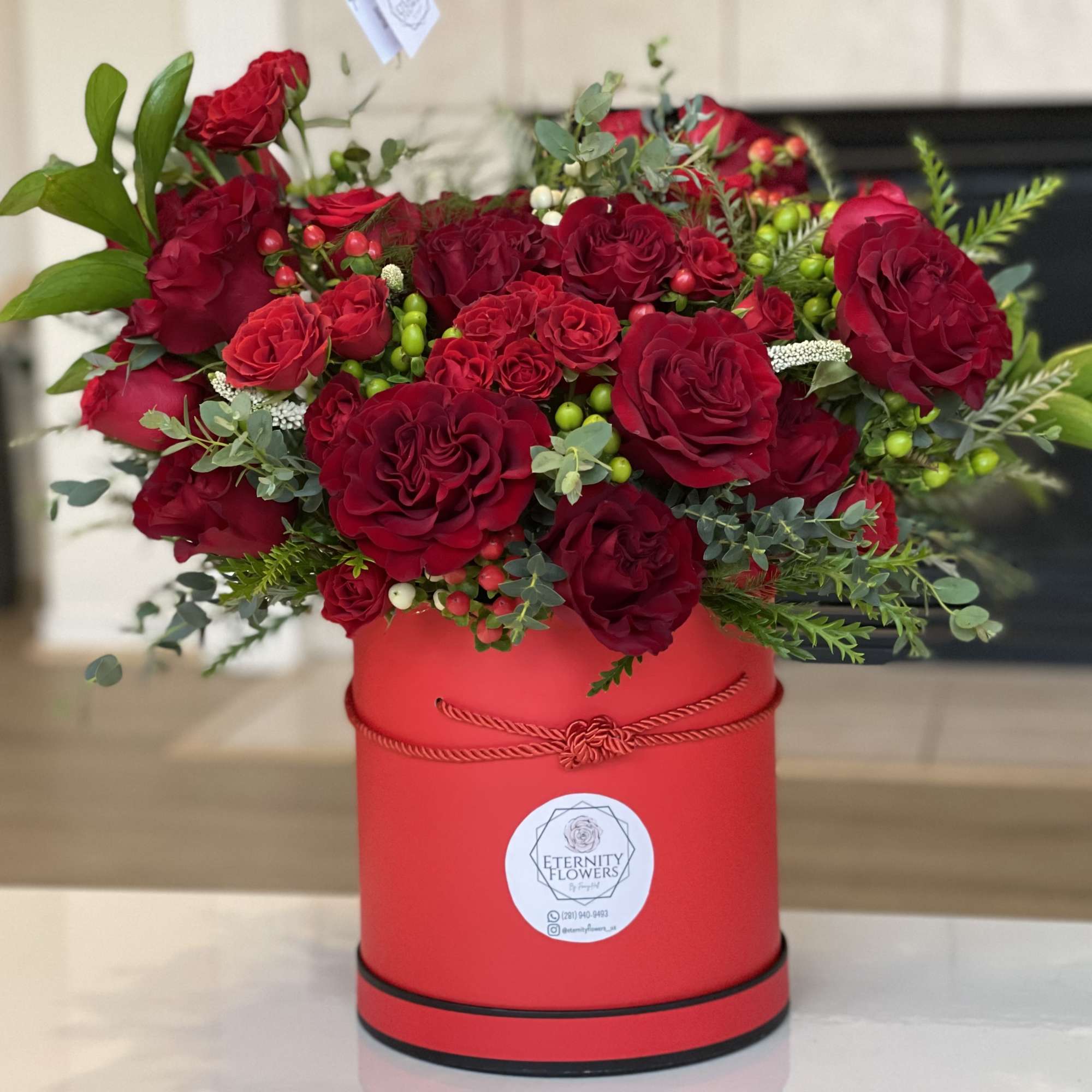 Red roses arranged in a red round box with greenery