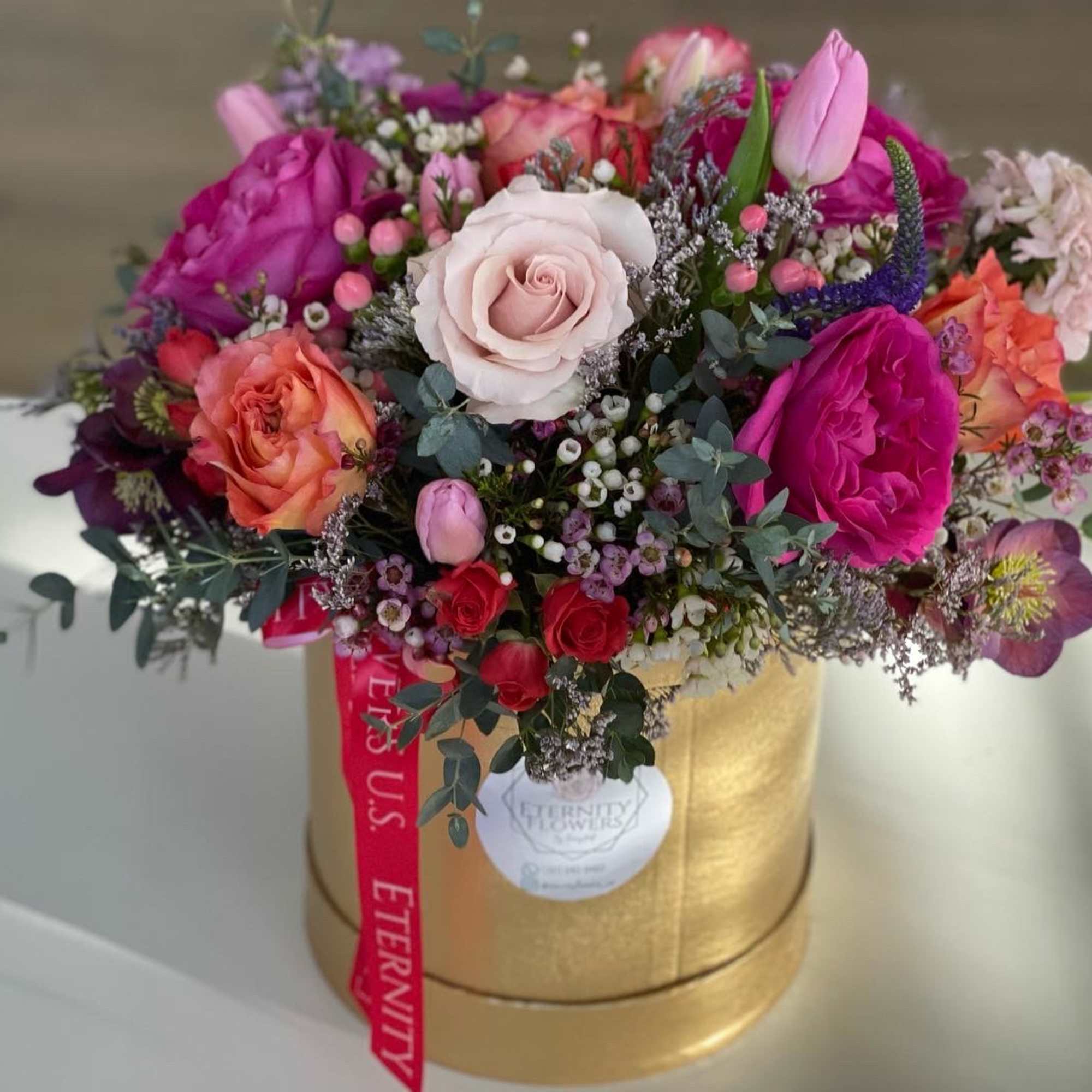 Mixed pink and peach roses in a gold hatbox