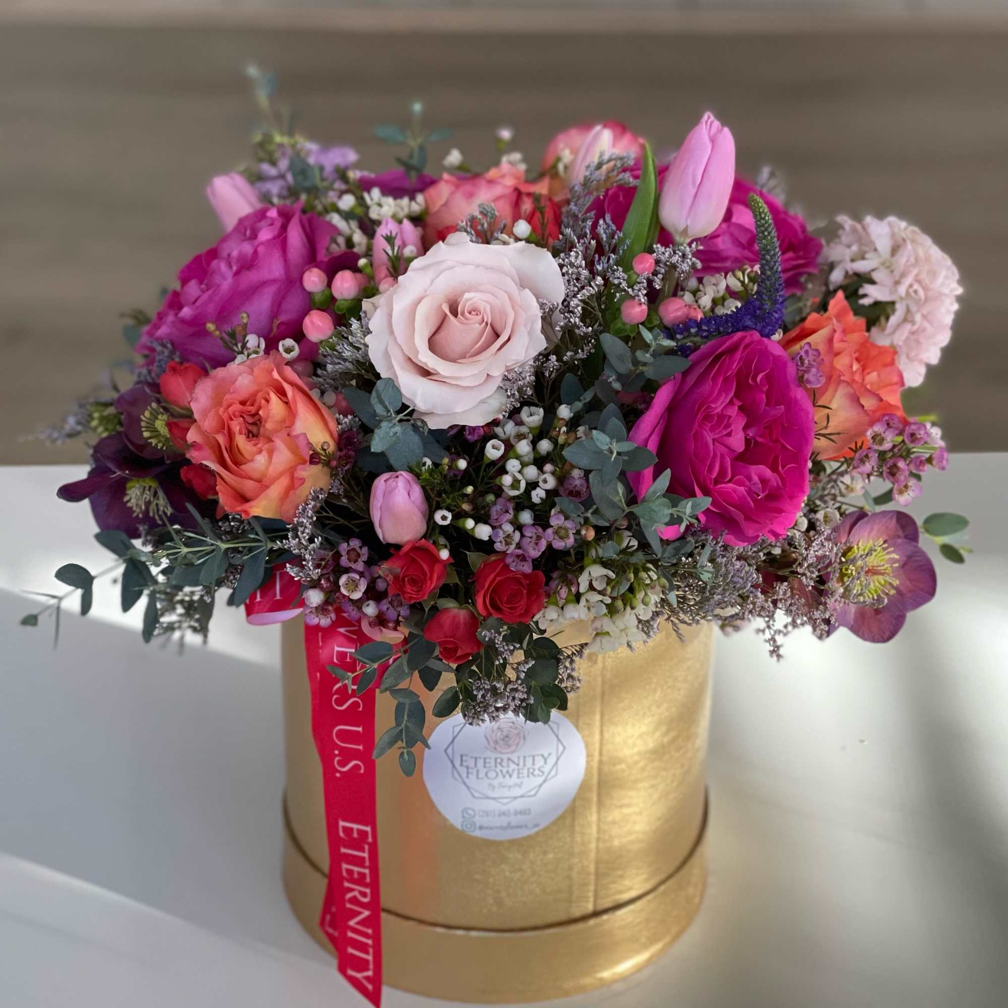 Mixed pink and peach roses in a gold hatbox with a ribbon