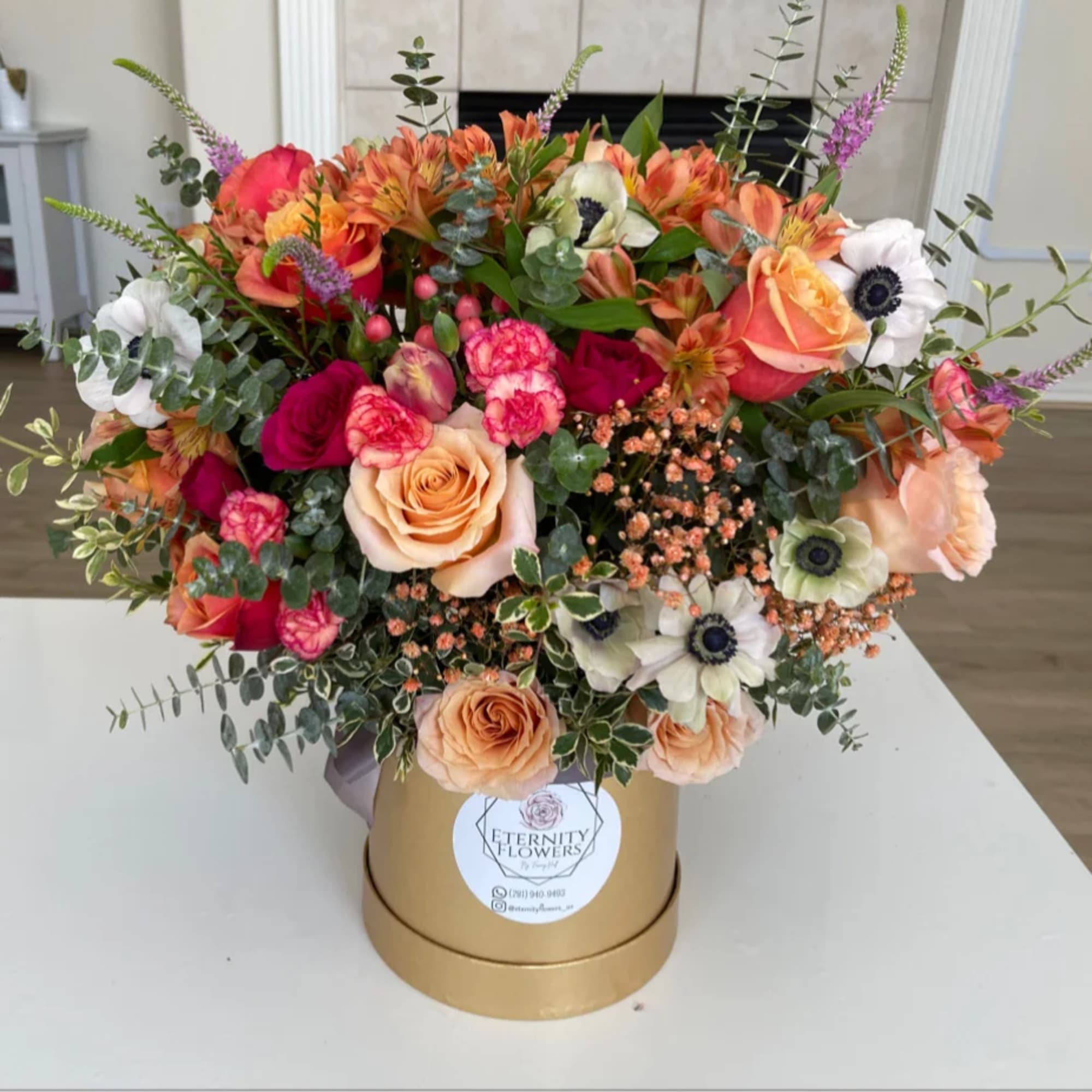 Mixed bouquet of roses, carnations, and anemones in a gold hatbox