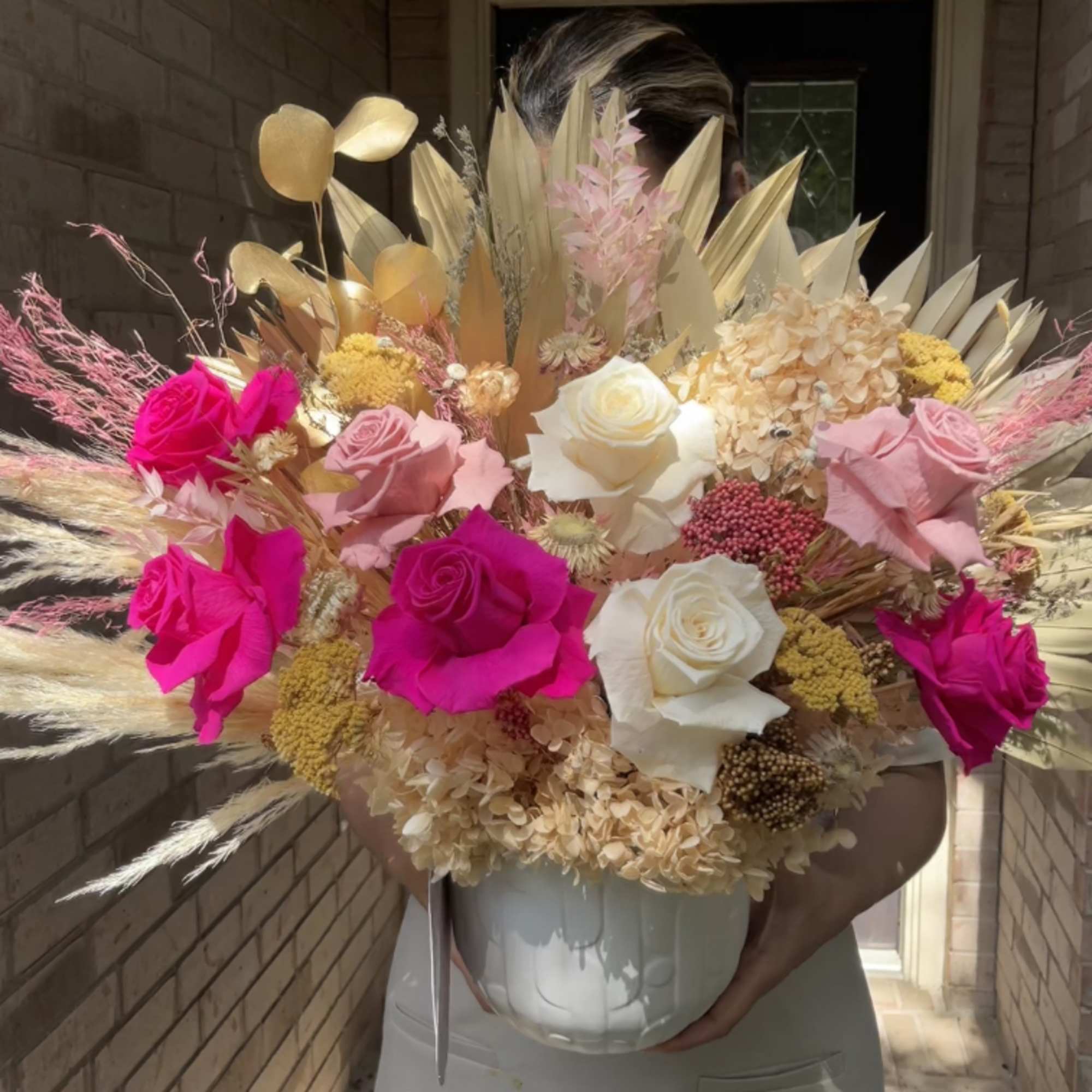 Large bouquet of pink and white roses with dried grasses in a white vase