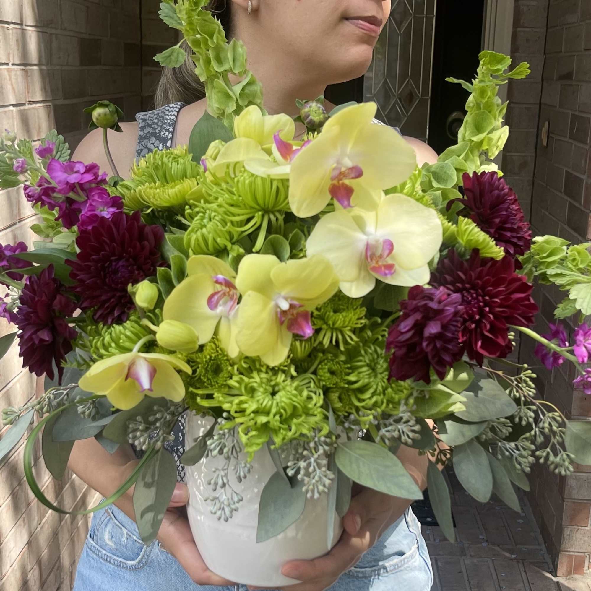 Bouquet of yellow orchids, green chrysanthemums, and burgundy blooms in a white vase