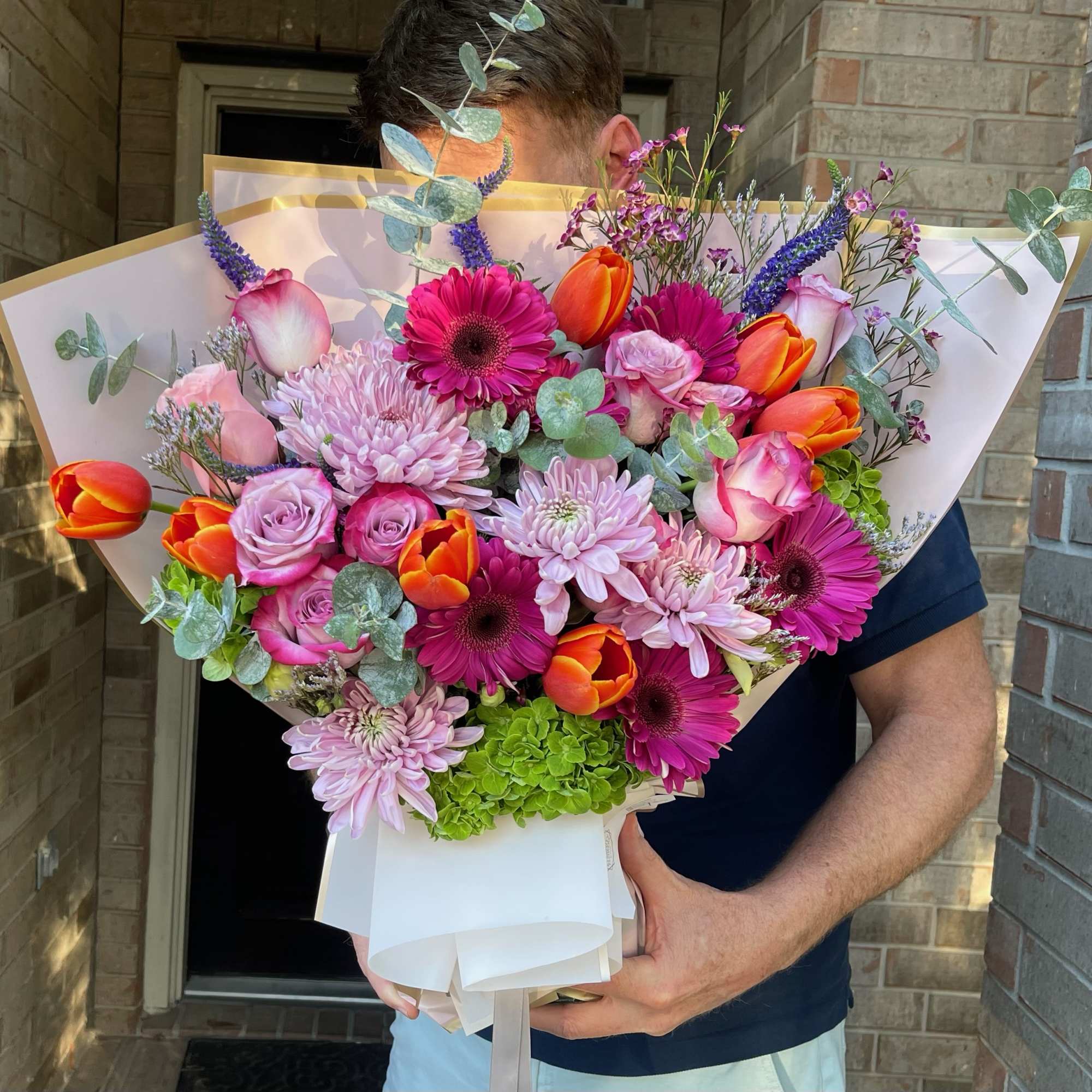 Large bouquet of pink, orange, and purple flowers wrapped in white paper