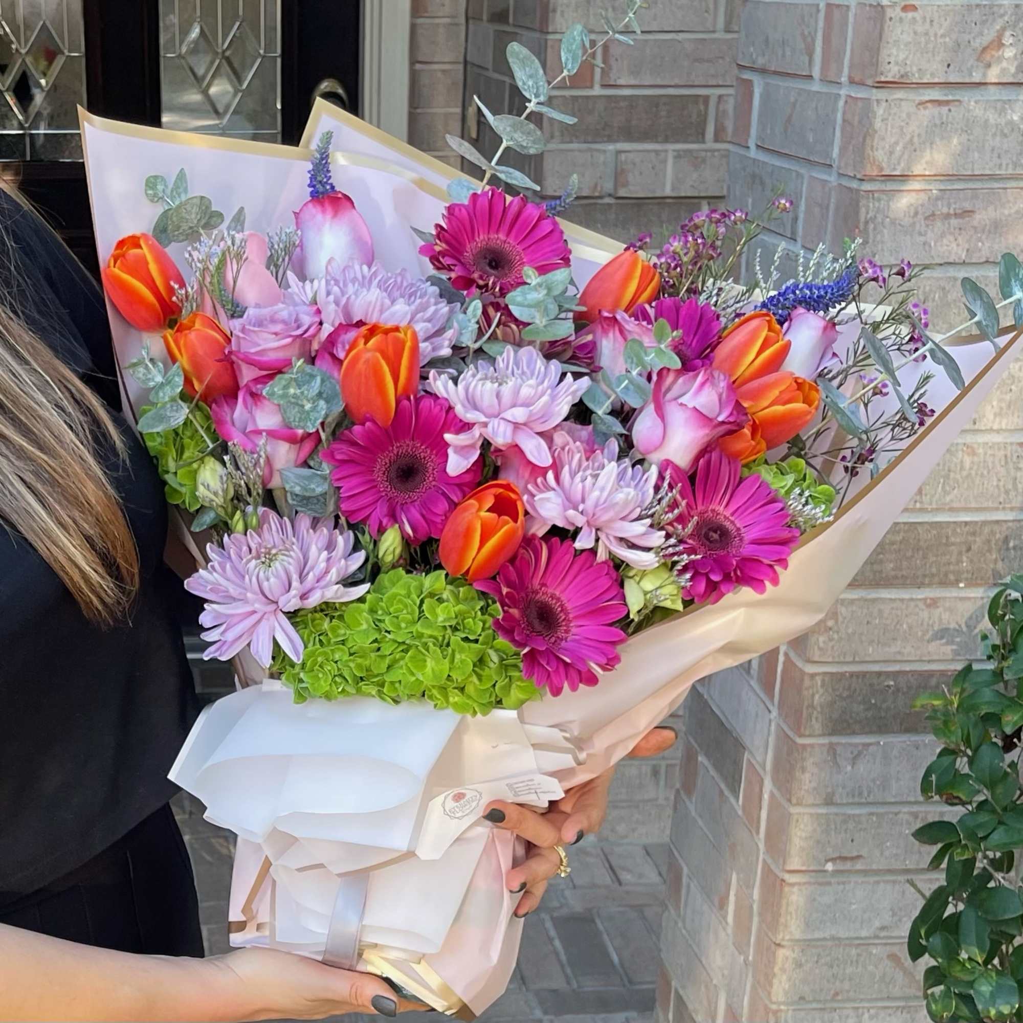 Handheld bouquet of pink gerberas, orange tulips, and lavender mums