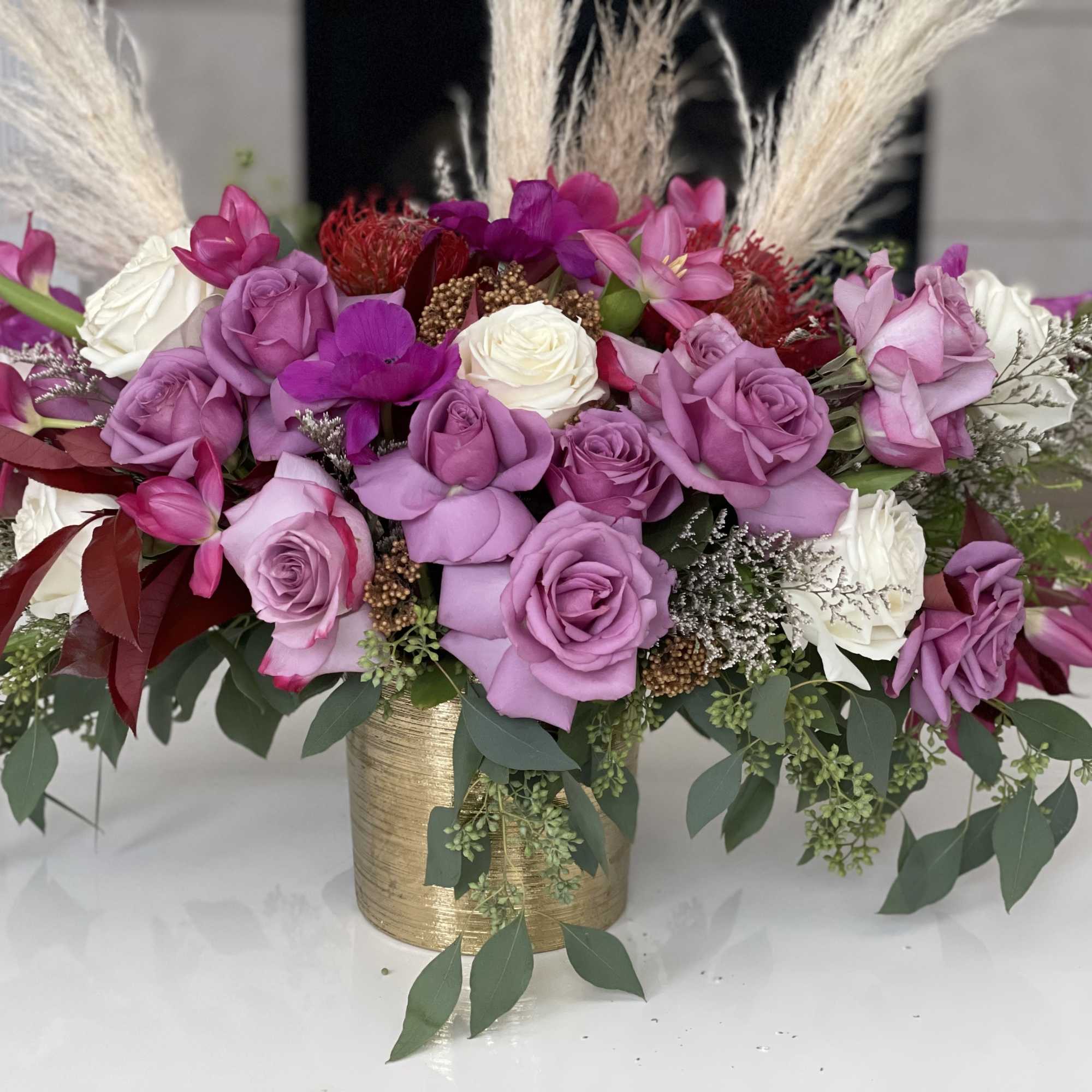 Pink and white roses arranged in a gold vase with tall pampas grass