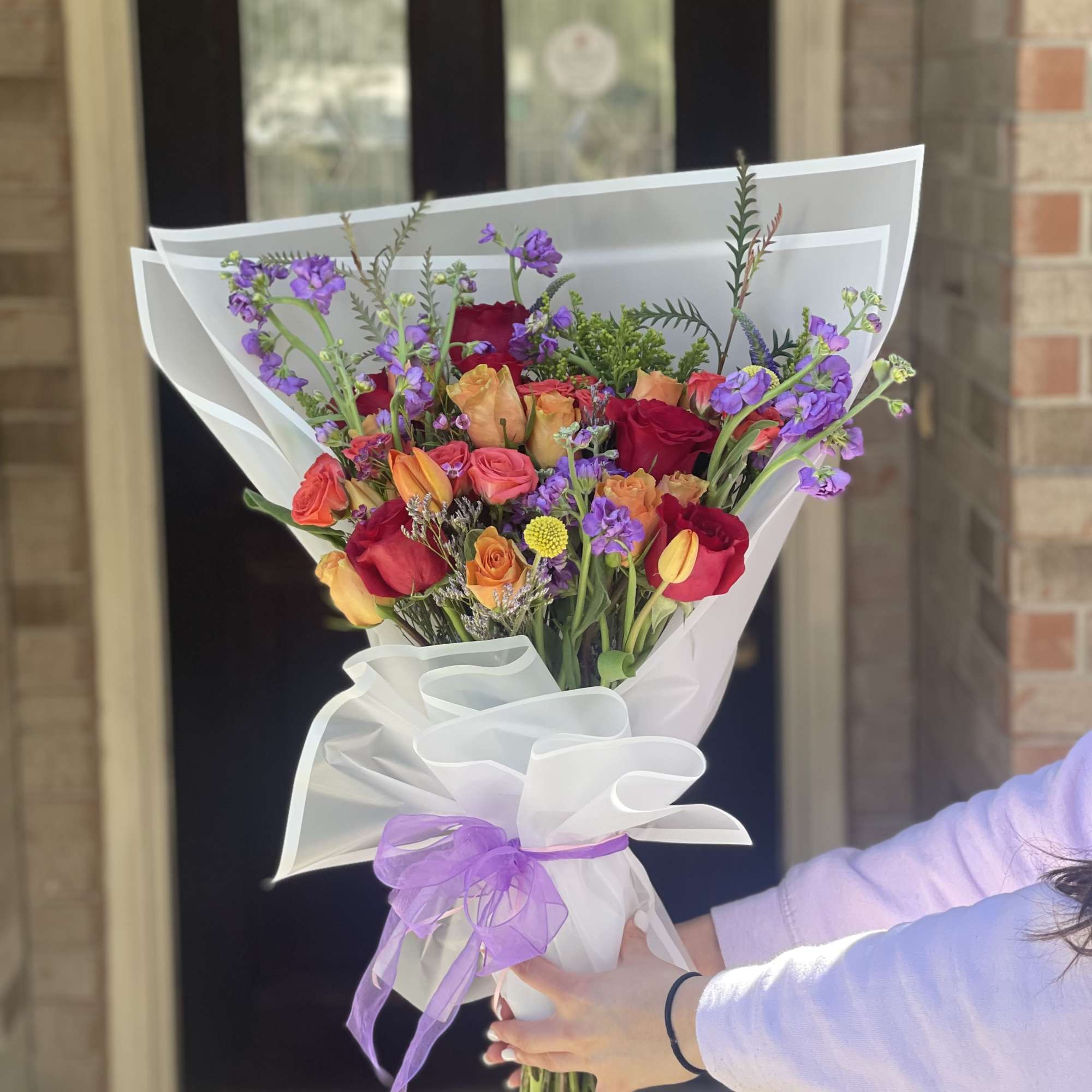 Hand-tied bouquet of red, orange, and purple flowers wrapped in white paper