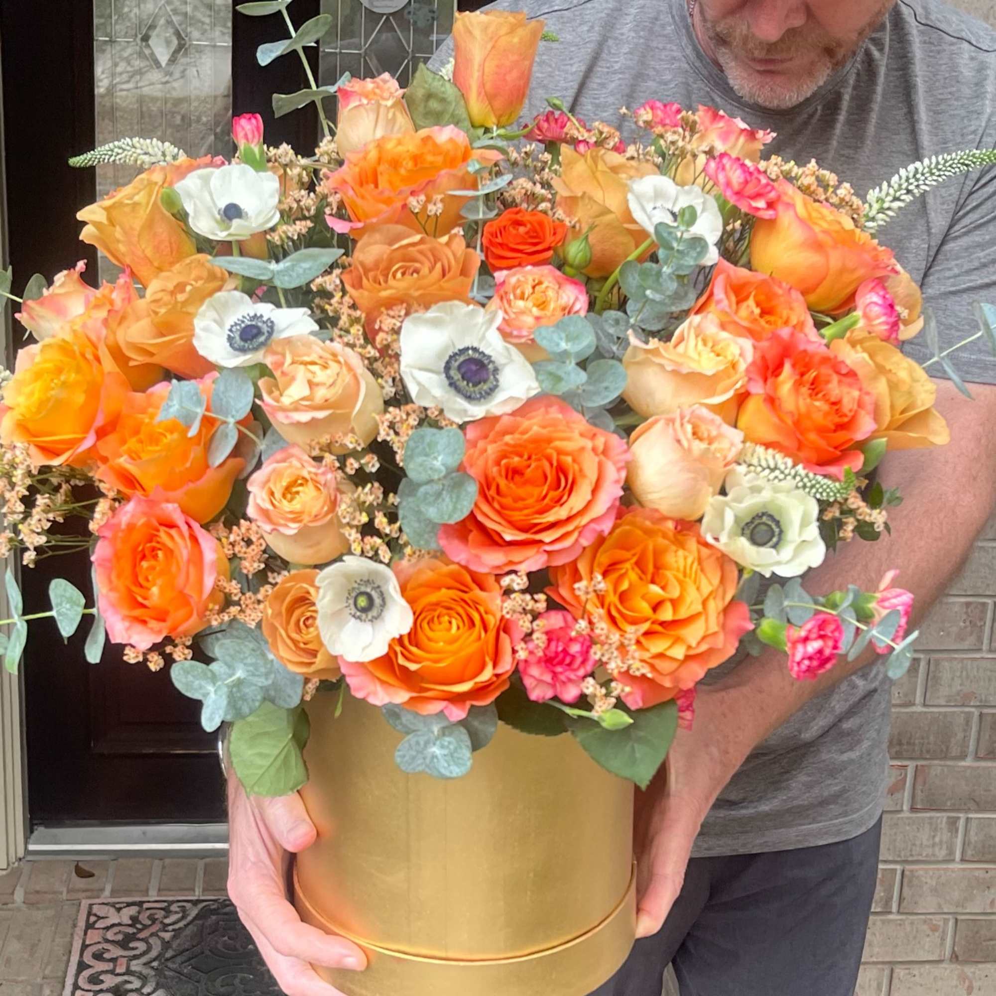 Large bouquet of orange and peach roses in a gold hatbox