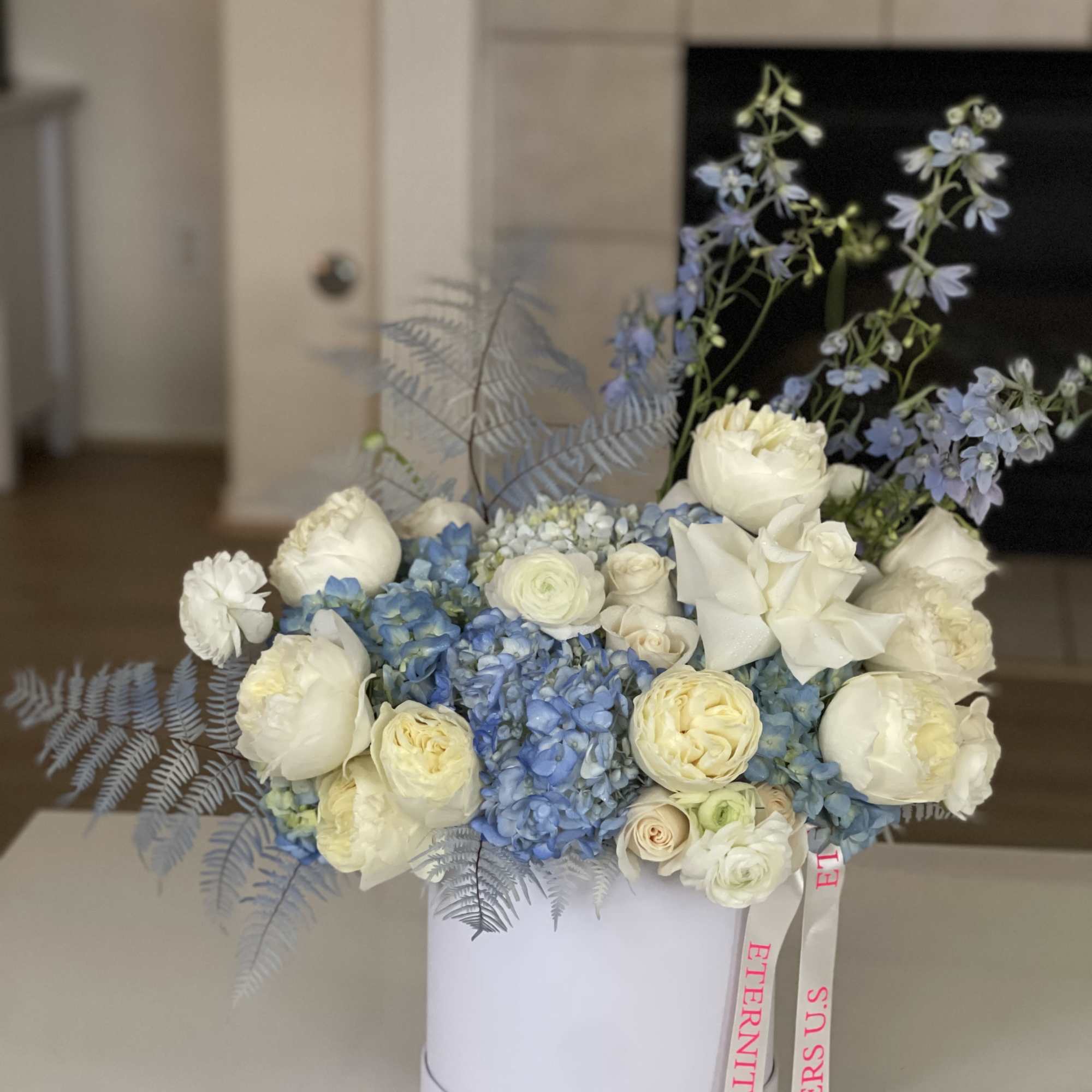 Blue and white floral arrangement in a white hat box with ribbon