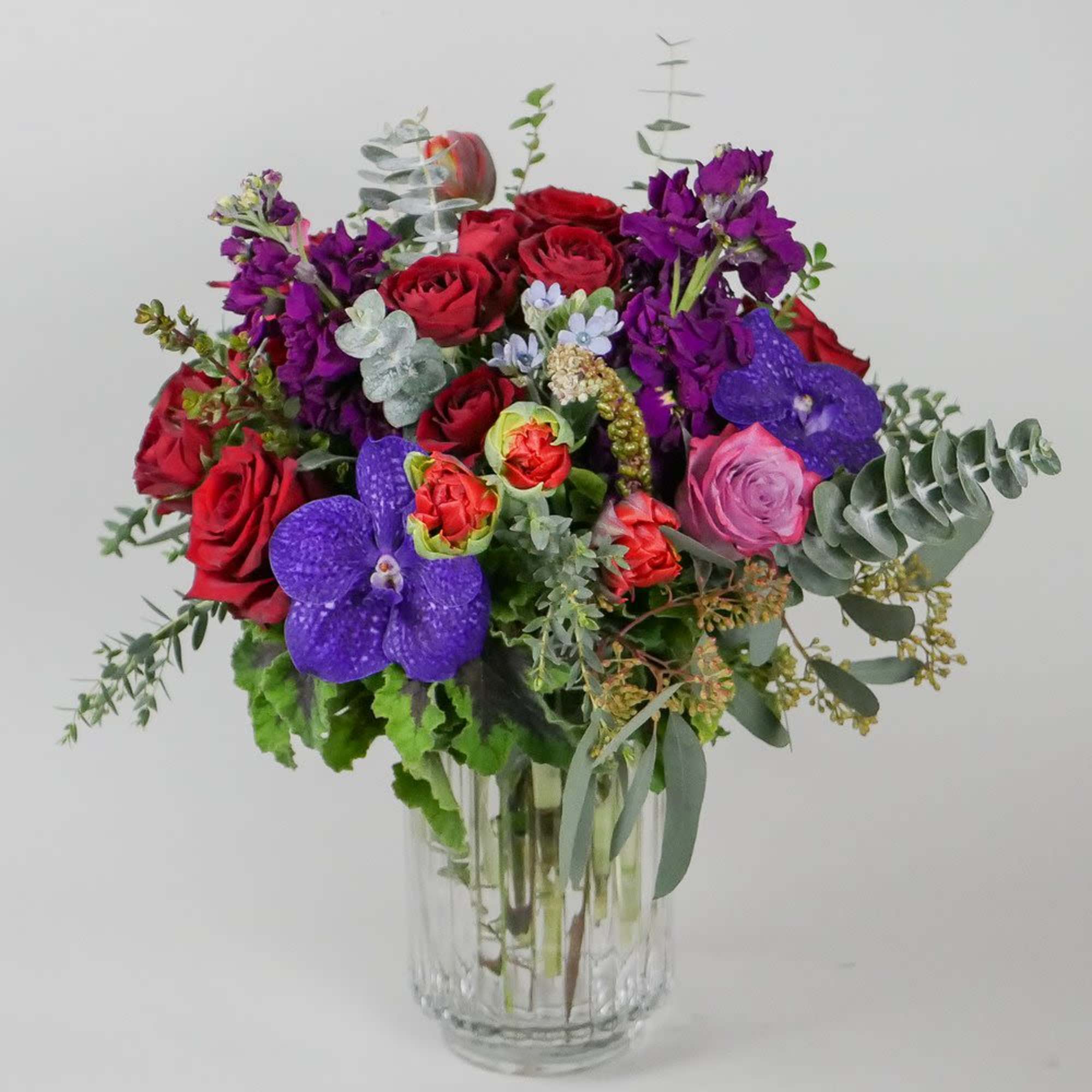 Bouquet of red roses and purple orchids in a clear glass vase