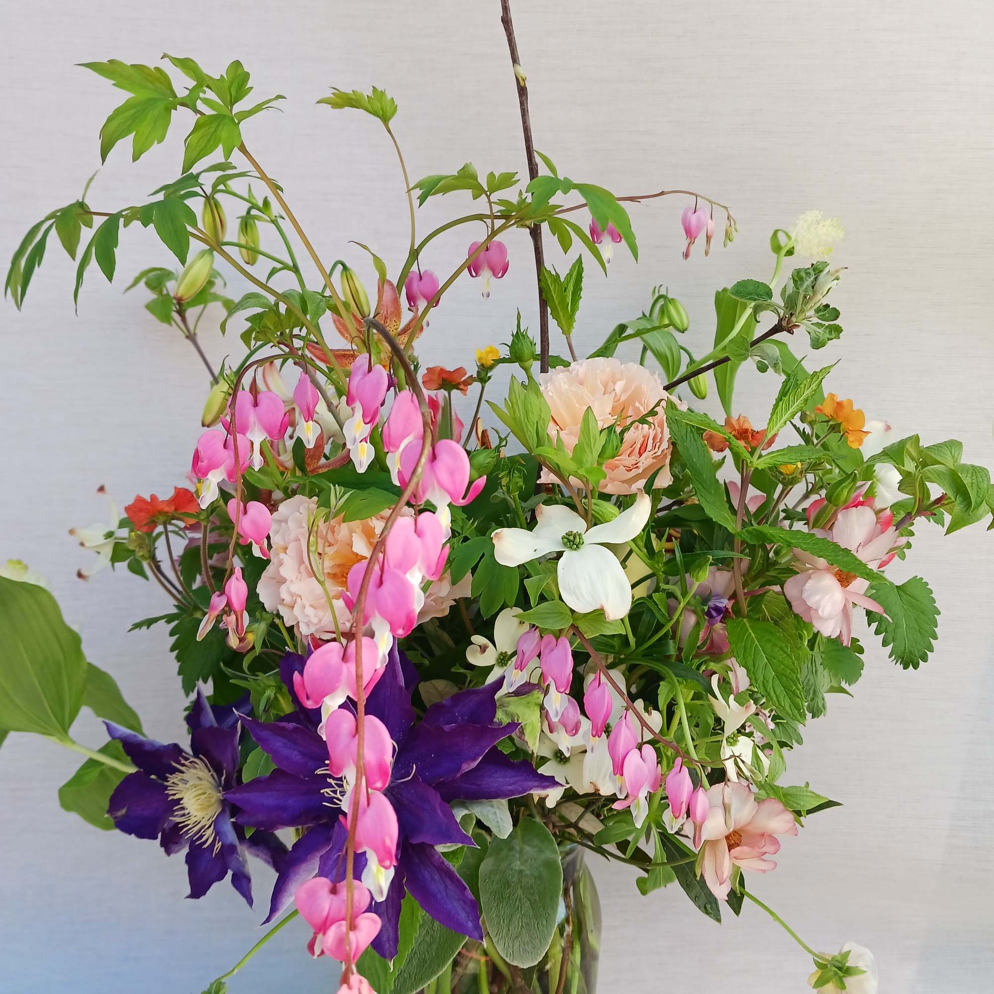 Loose garden-style bouquet of pink, purple, and peach flowers in a clear glass vase