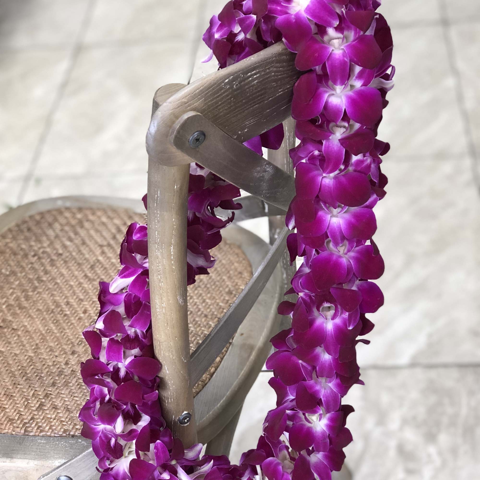Purple orchid flower lei draped over the back of a wooden chair