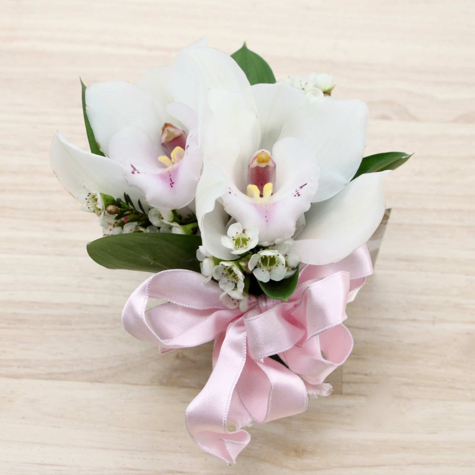 White orchid corsage with pink centers, tiny white blooms, and a pink ribbon bow