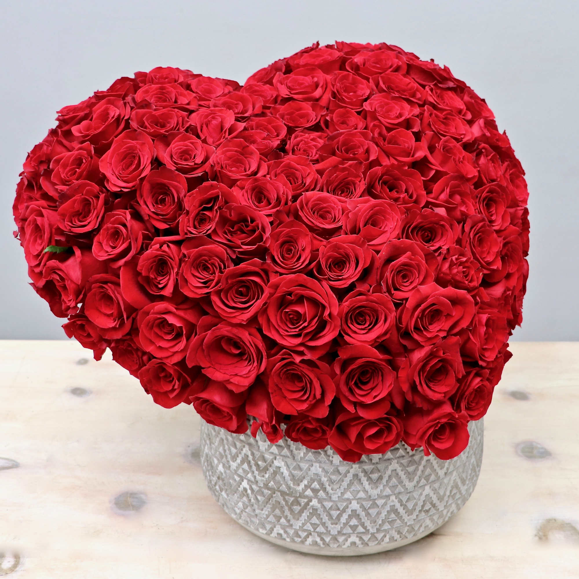 Heart-shaped arrangement of red roses in a patterned ceramic pot