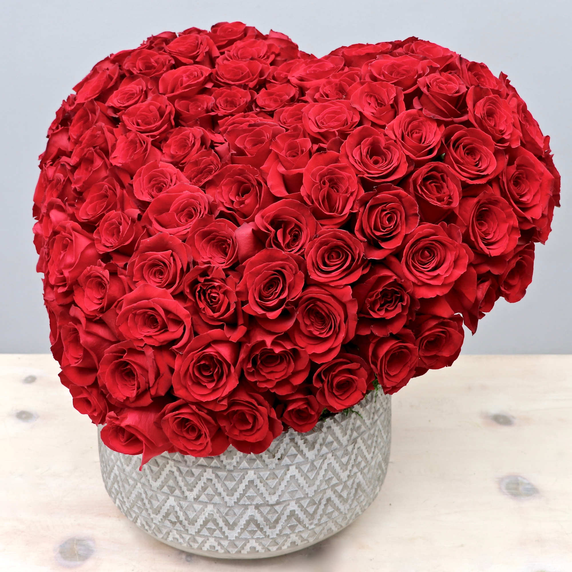 Heart-shaped arrangement of red roses in a white patterned ceramic container