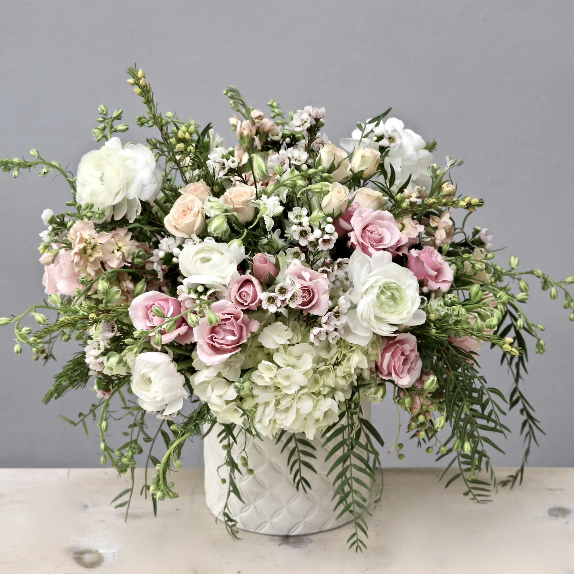 Soft white and pink flower arrangement in a white textured ceramic vase