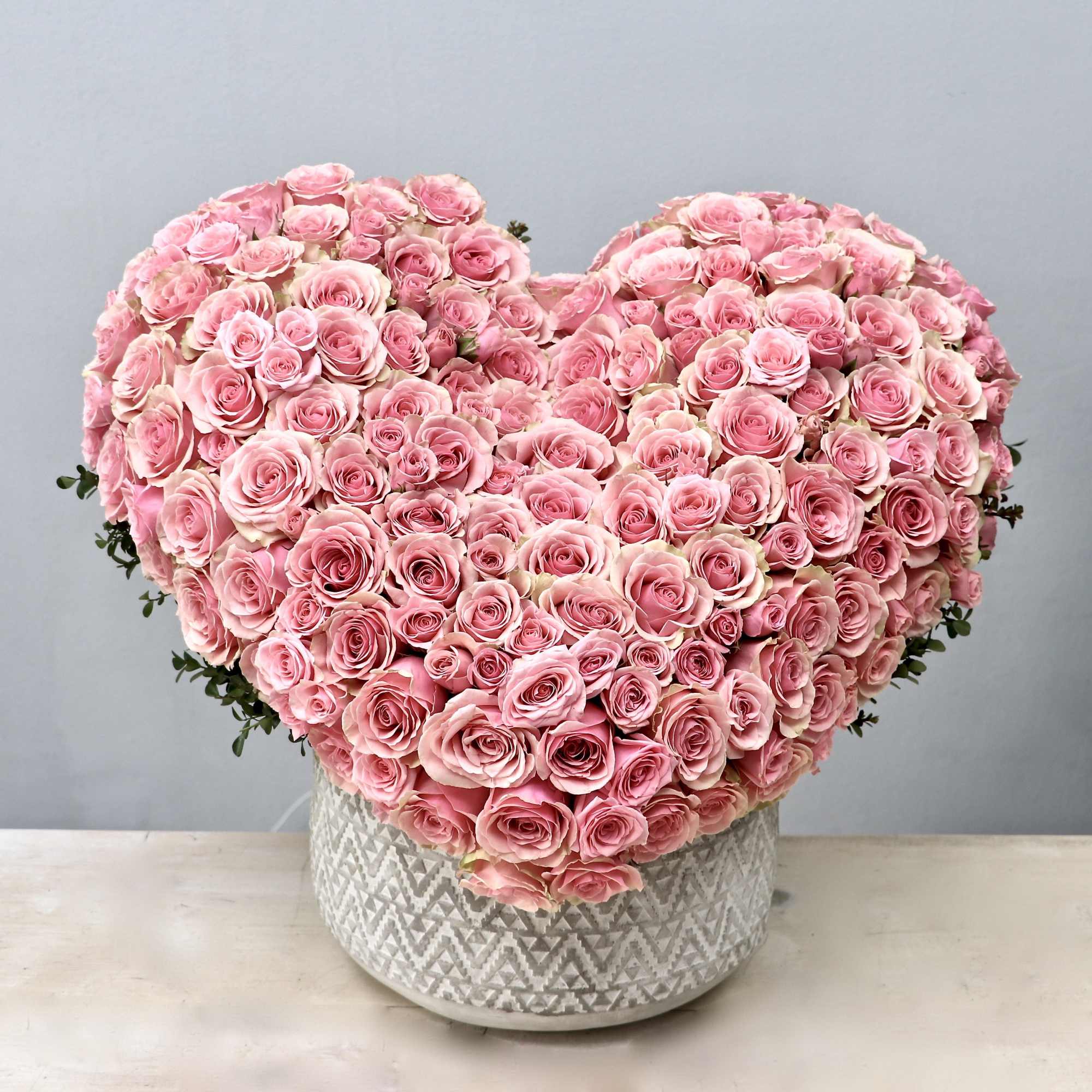 Heart-shaped arrangement of pink roses in a patterned white ceramic pot