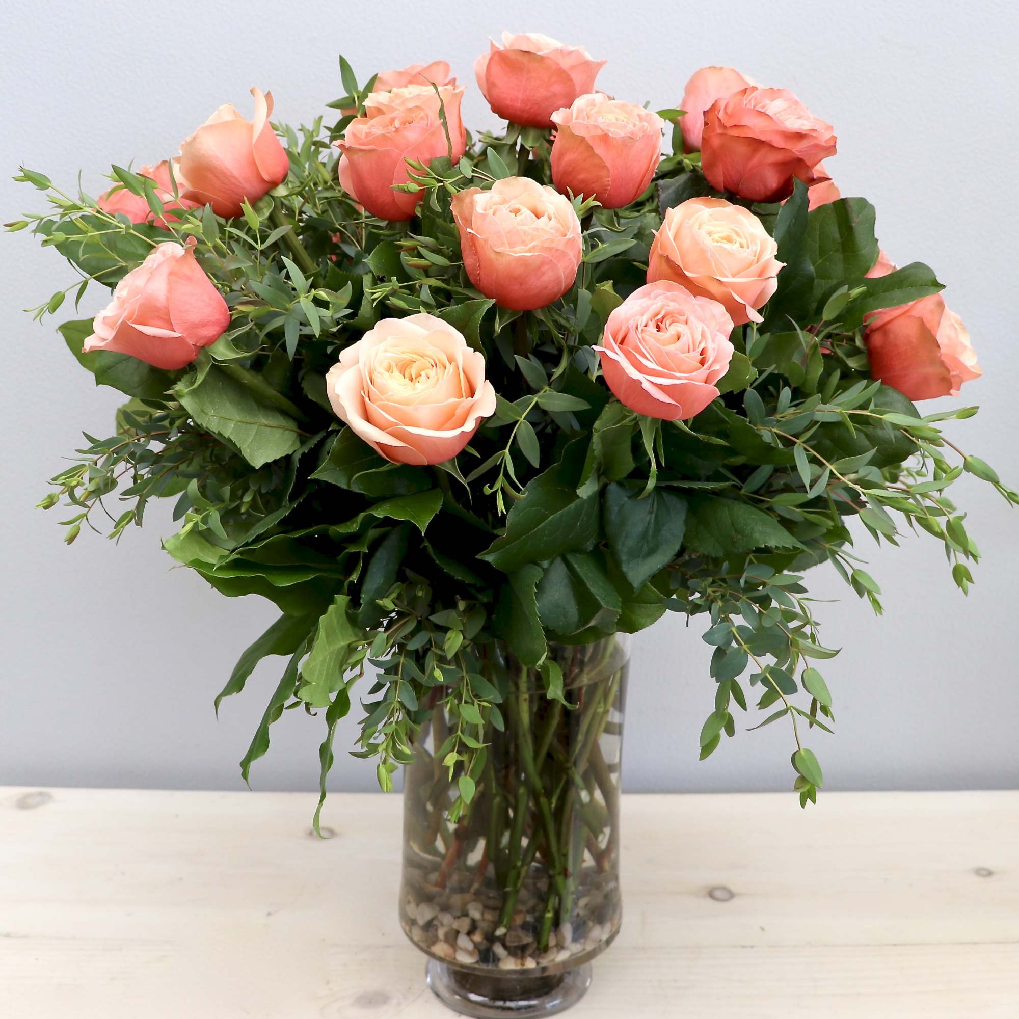 Arrangement of peach roses in a clear glass vase with stones