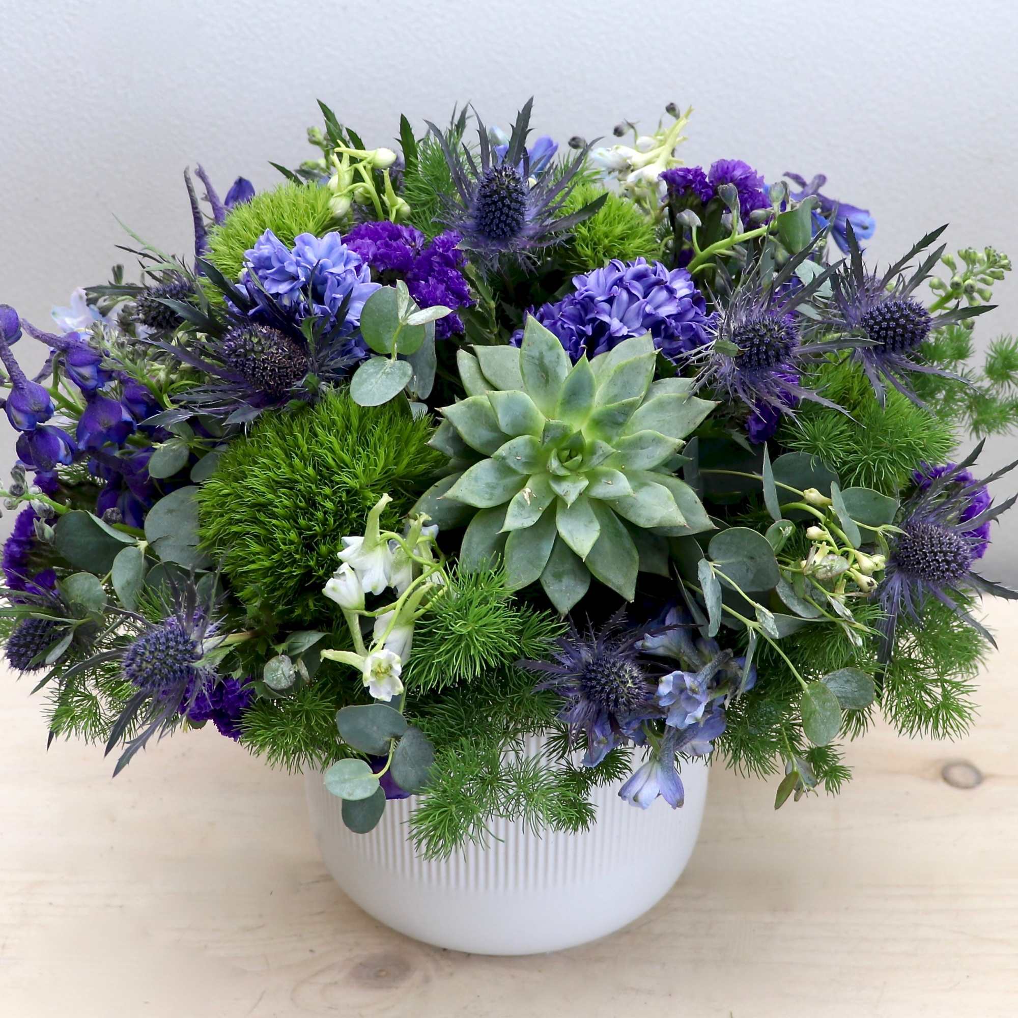 Low arrangement of green succulent and purple-blue flowers in a white ceramic pot