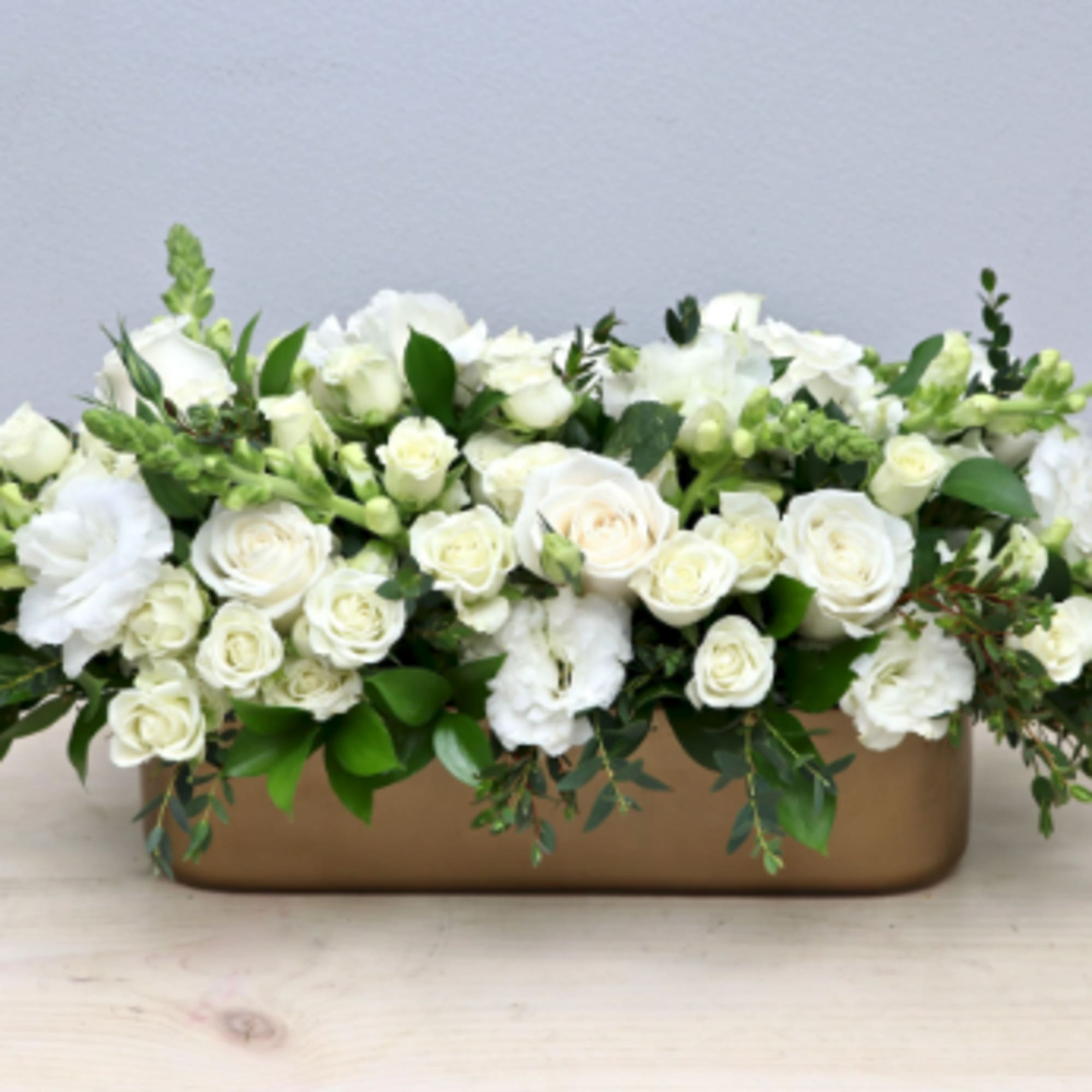 Low rectangular arrangement of white roses and blooms in a gold container