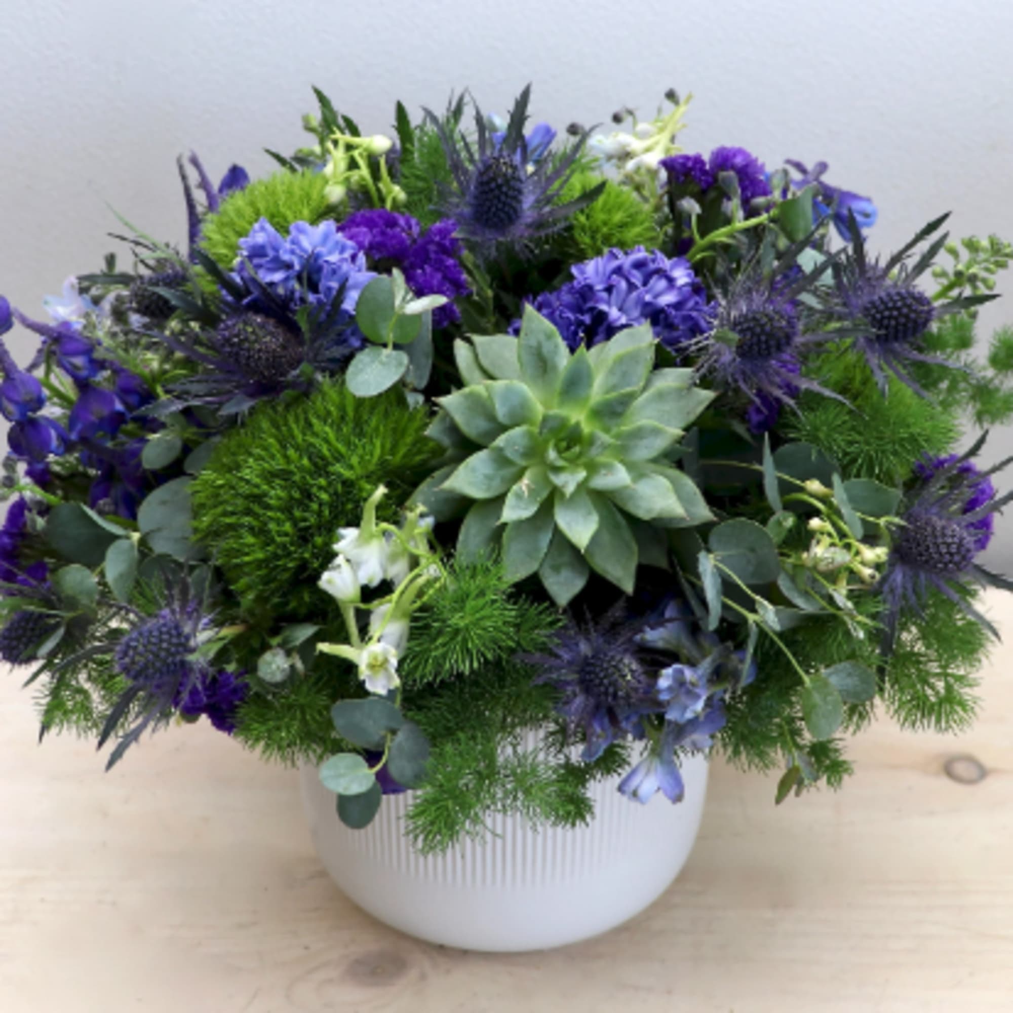 Low purple and green arrangement with succulents and mixed flowers in a white ceramic pot