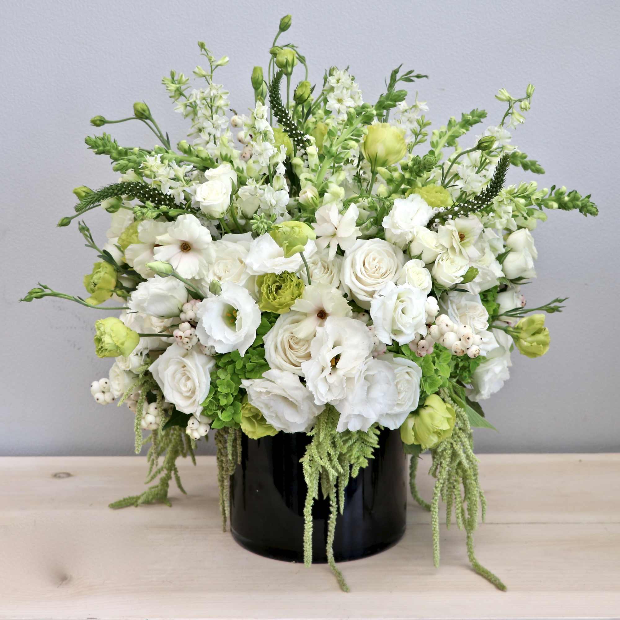 White and green flower arrangement with roses and lisianthus in a black cylinder vase
