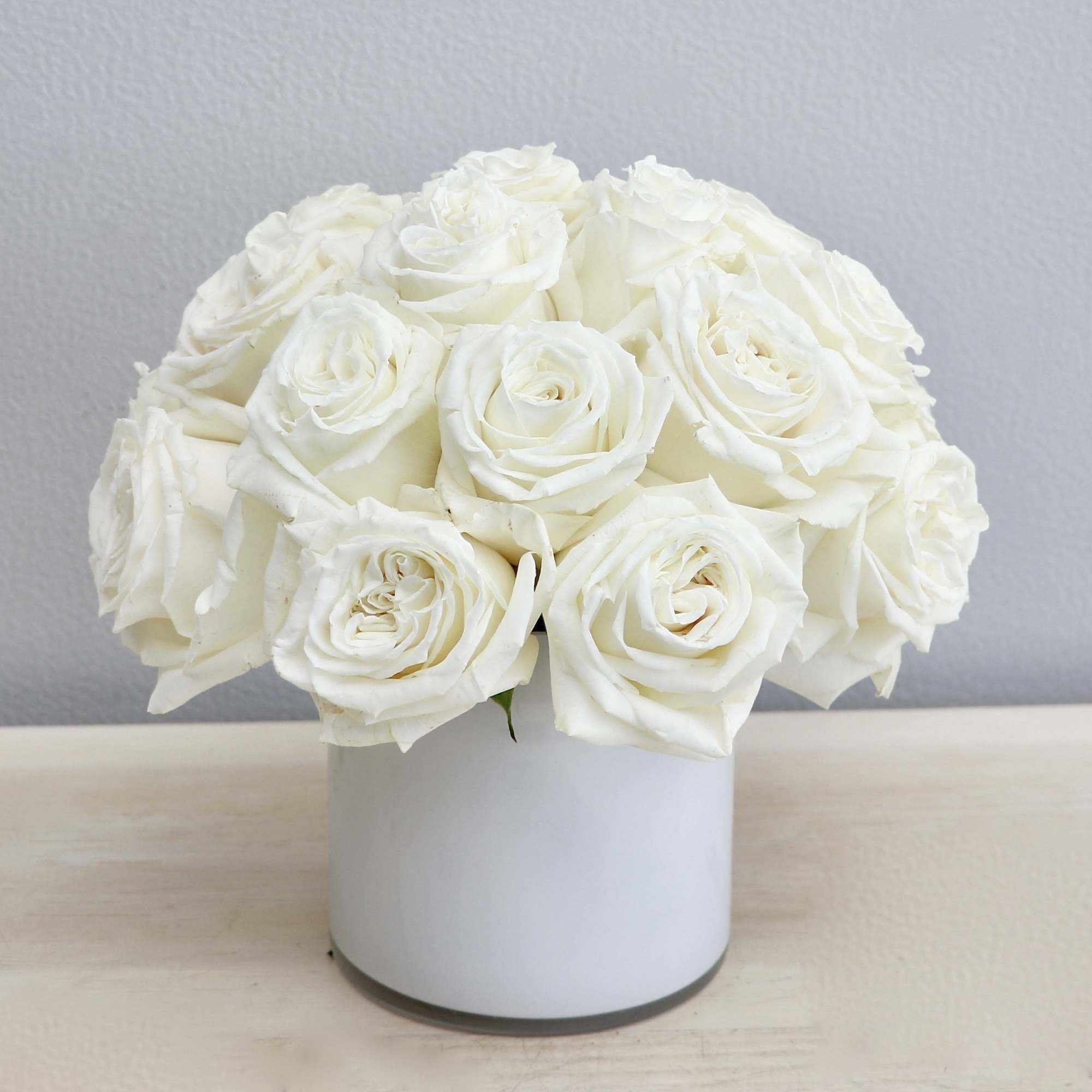 Compact arrangement of white roses in a white cylinder vase