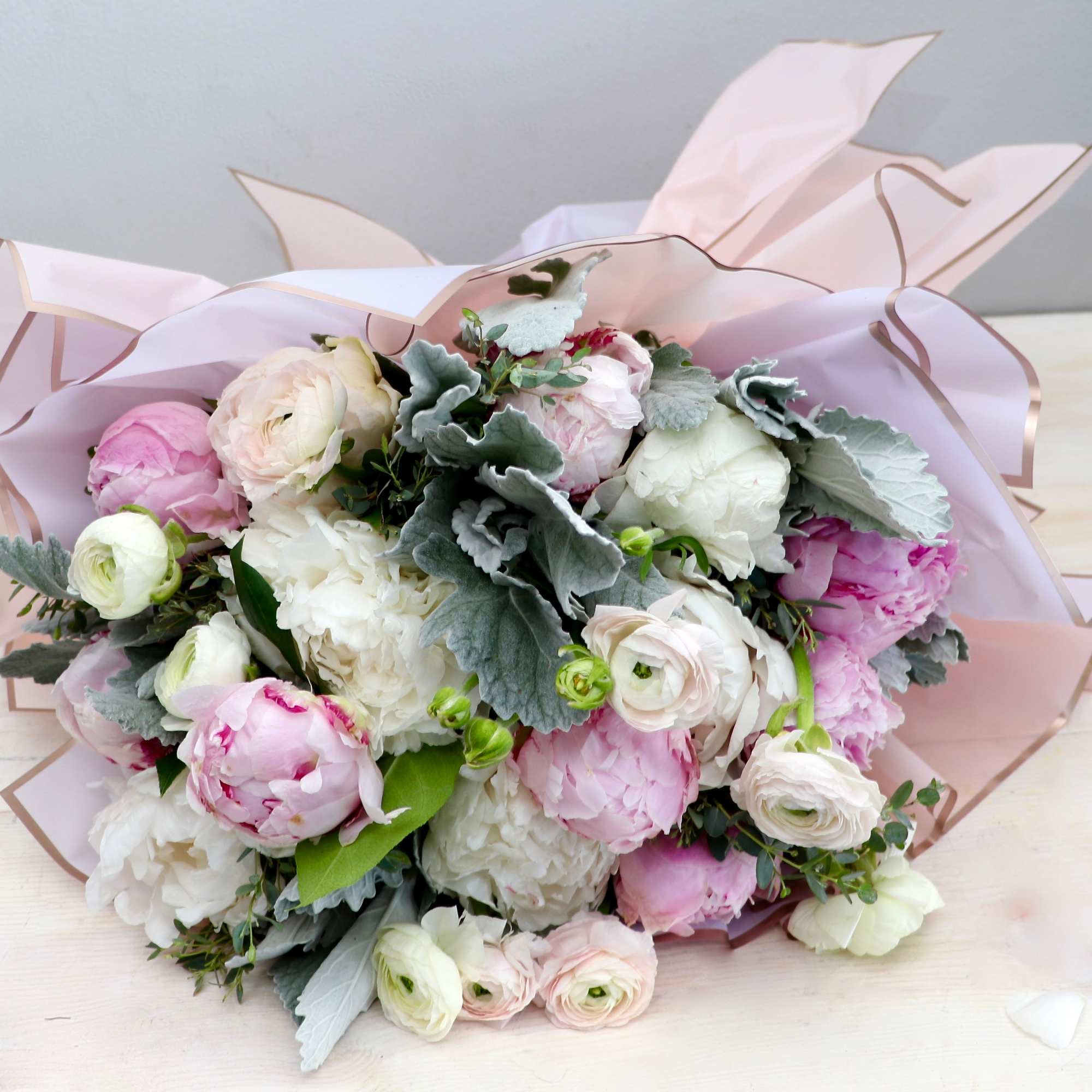 Hand-tied bouquet of white and blush pink peonies and ranunculus wrapped in pale pink paper