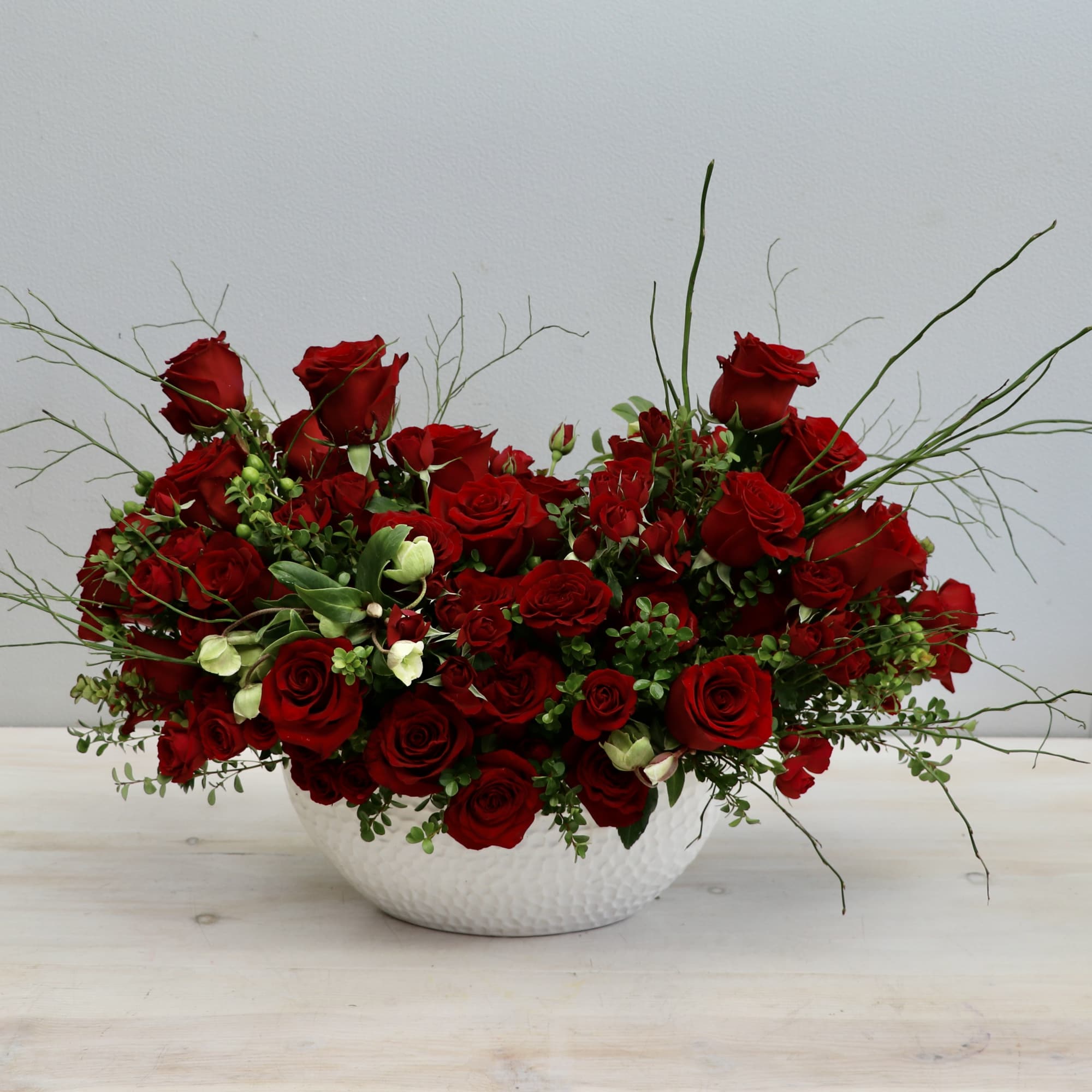 Low centerpiece of red roses with wispy greenery in a white textured bowl