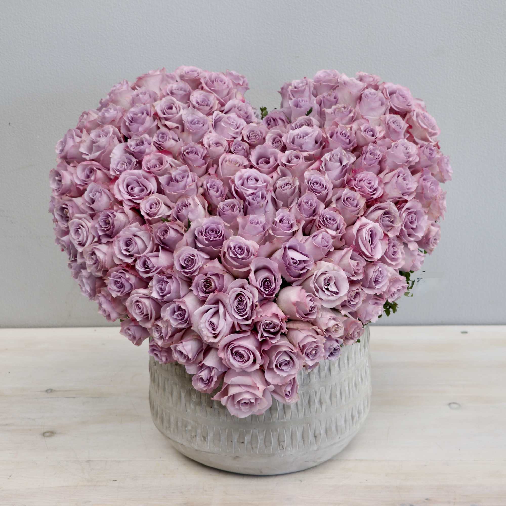 Heart-shaped arrangement of light lavender roses in a white ceramic pot