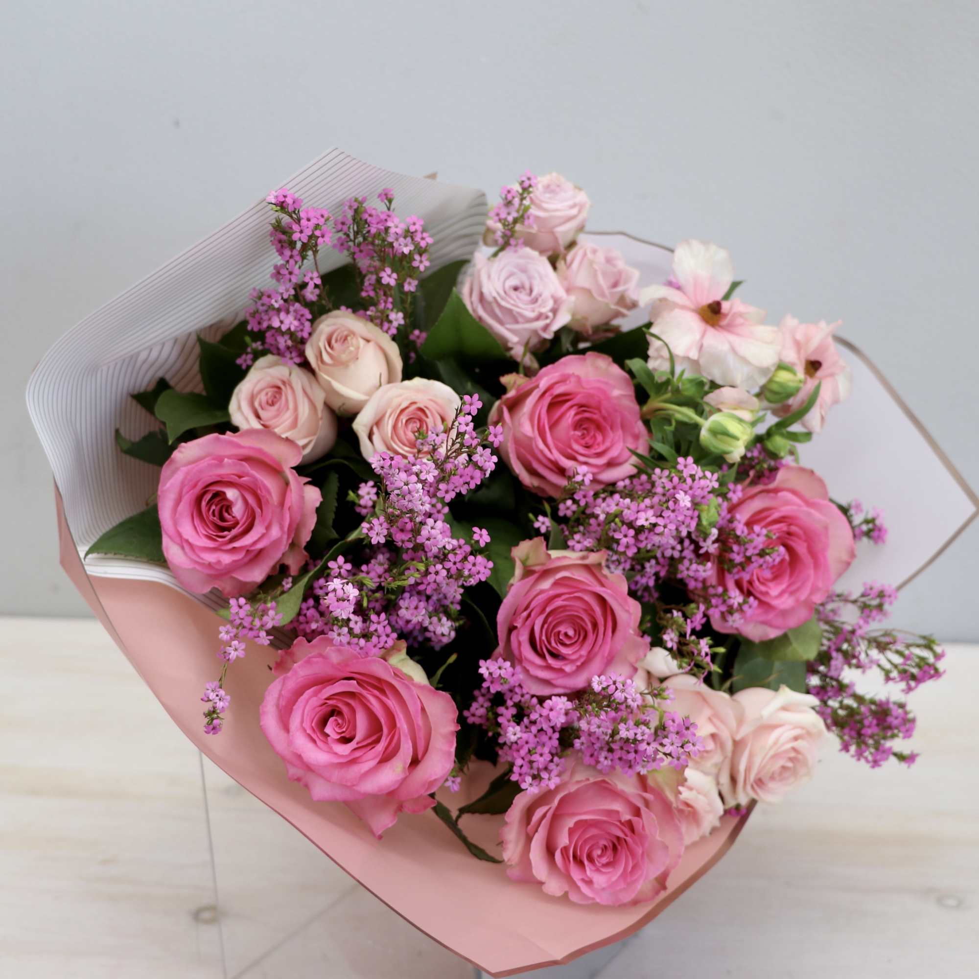 Hand-tied bouquet of hot pink and pale pink roses with small pink filler flowers in pink paper wrap