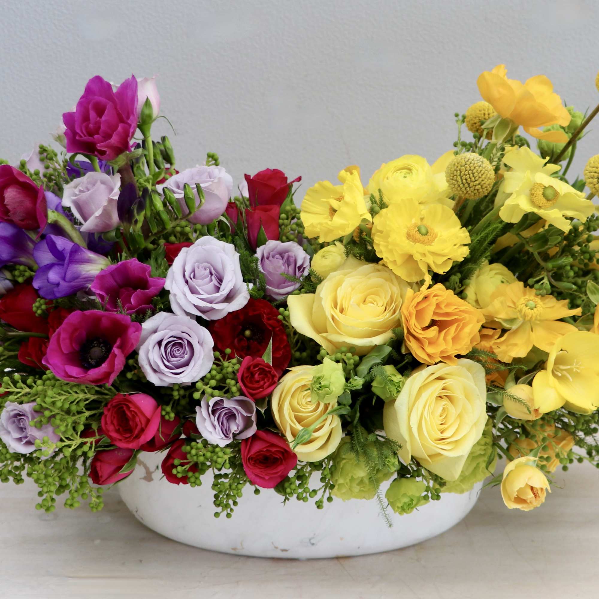 Low centerpiece of purple, pink, red, and yellow flowers in a white oval bowl
