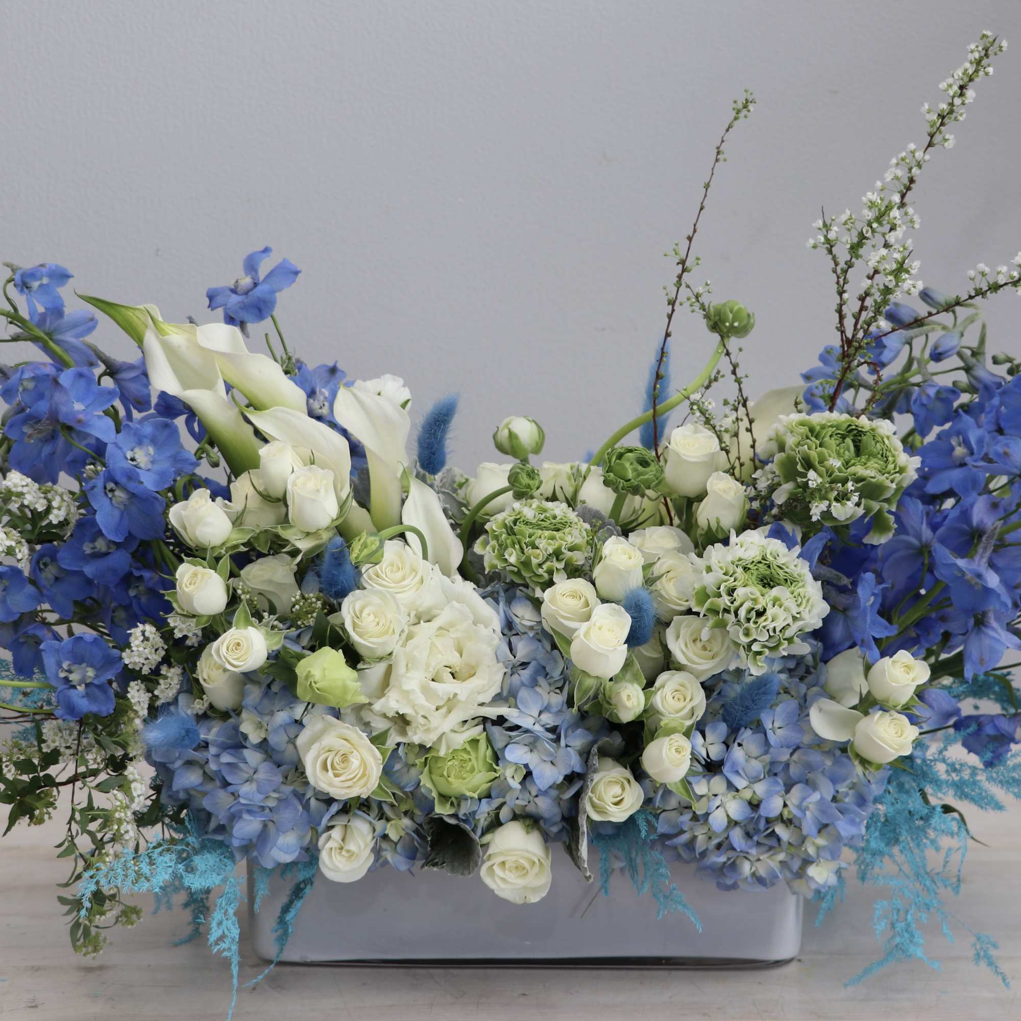 Low blue and white flower arrangement with roses, hydrangeas and calla lilies in a rectangular white container