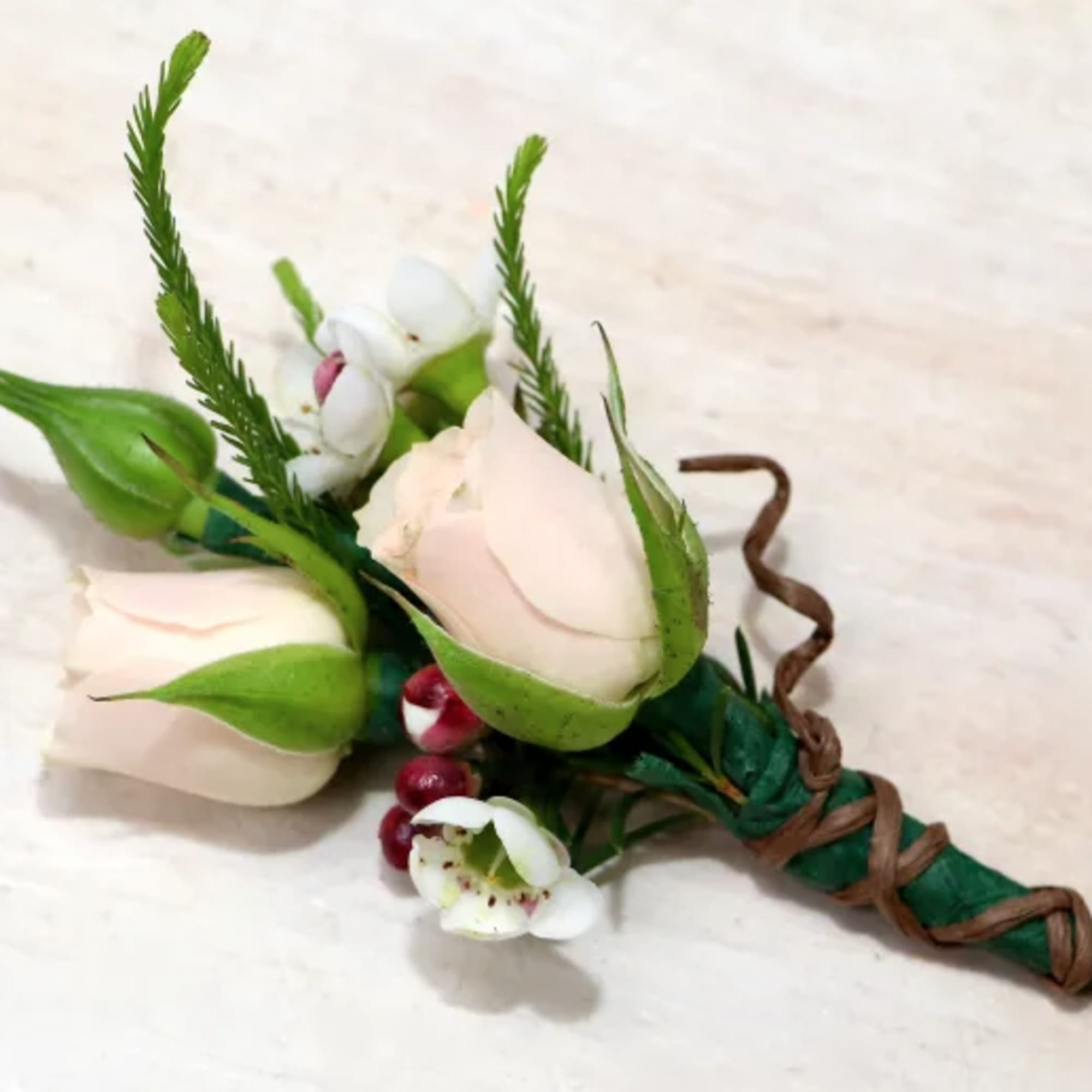 Boutonniere with blush rosebuds, white blooms, and red berries wrapped with twine