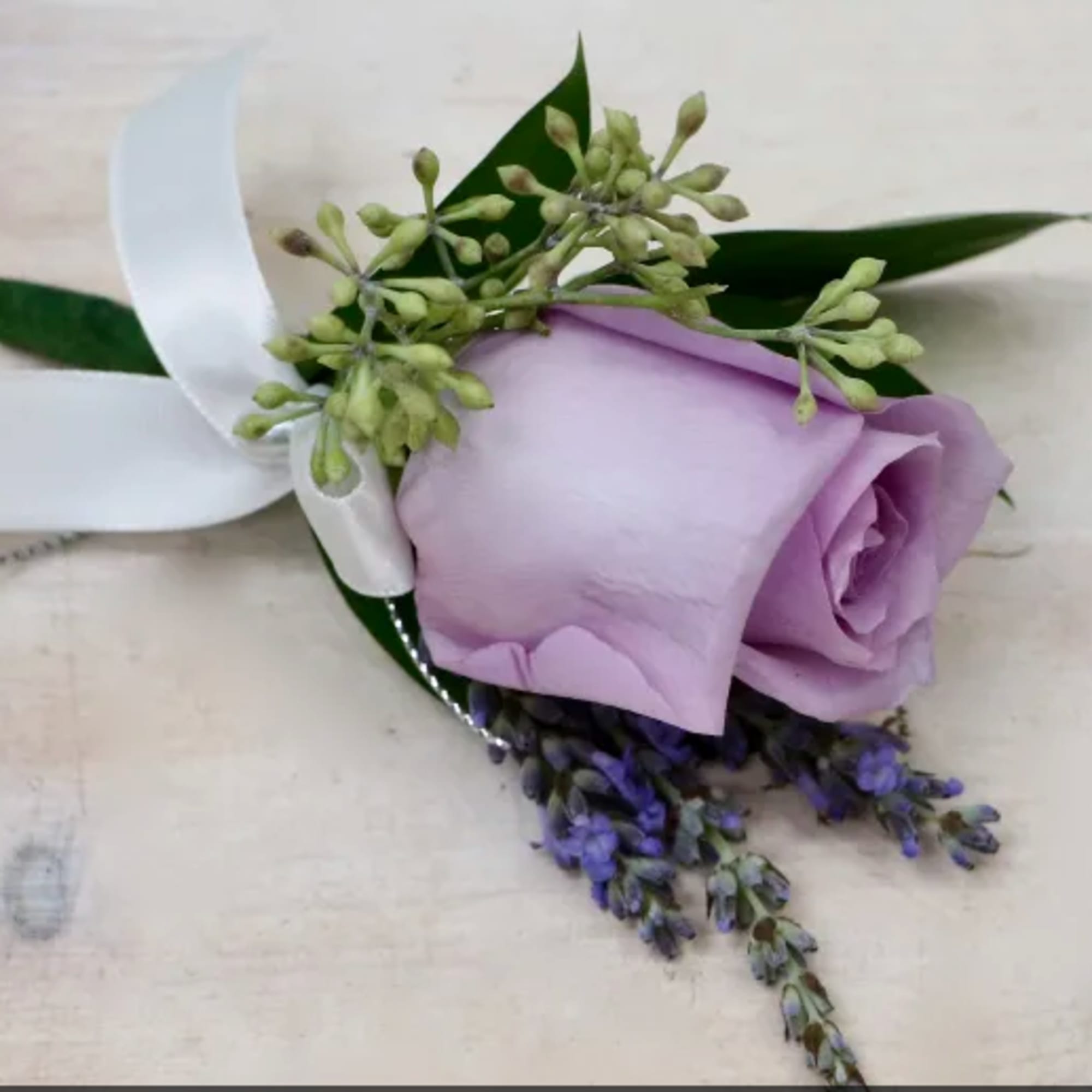 Lavender rose boutonniere with small purple blooms and a white ribbon bow